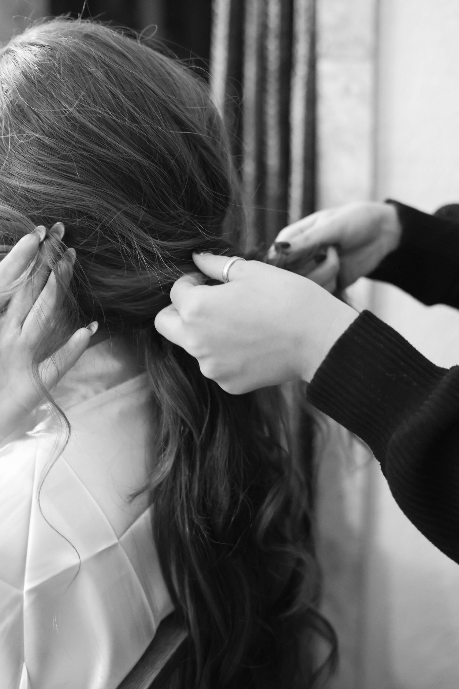 Hands styling long dark hair during wedding preparation.