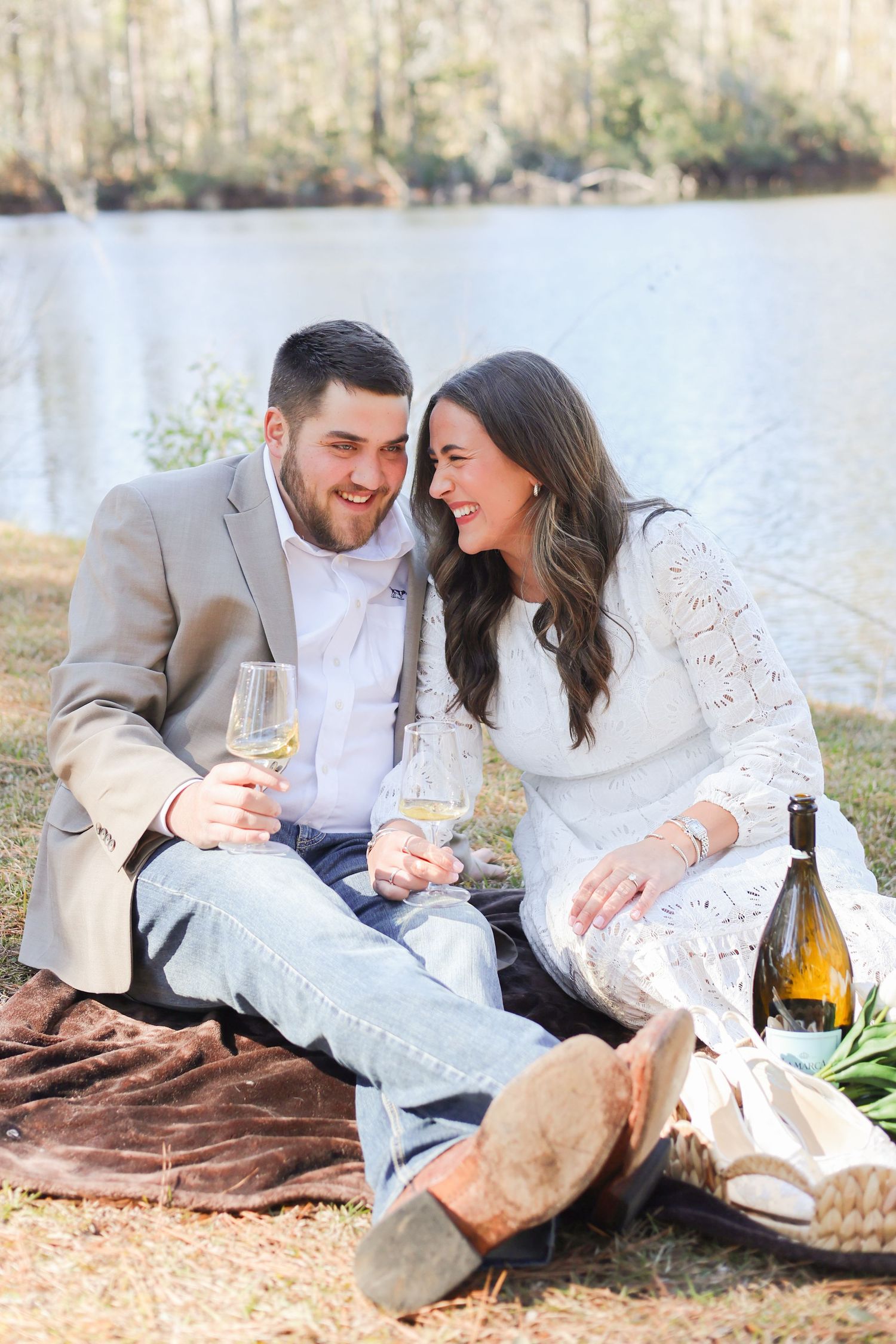 Couple enjoys romantic picnic with wine by lakeside on brown blanket during autumn afternoon.