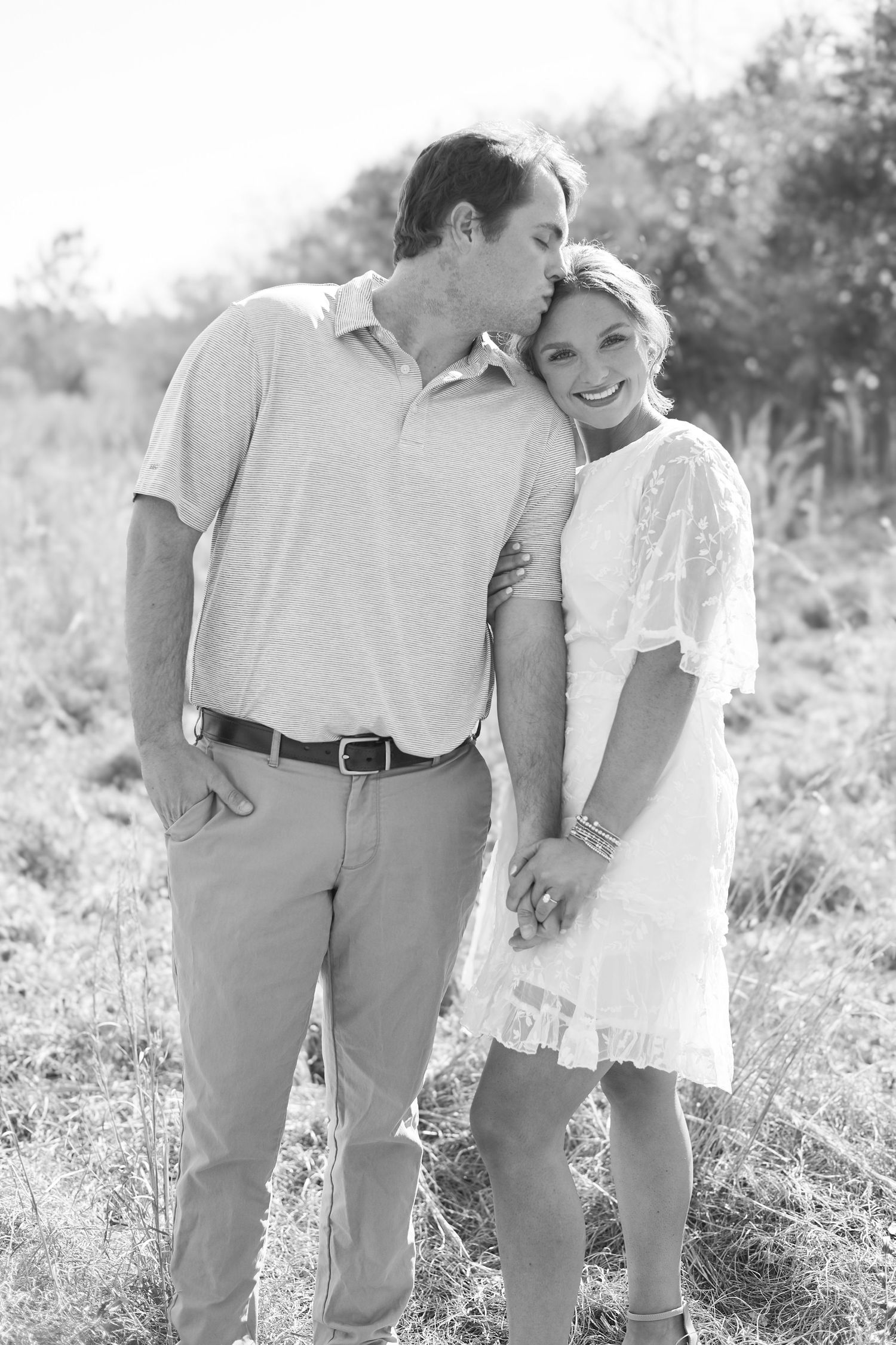 Black and white portrait of a couple in casual attire embracing outdoors in a natural setting.