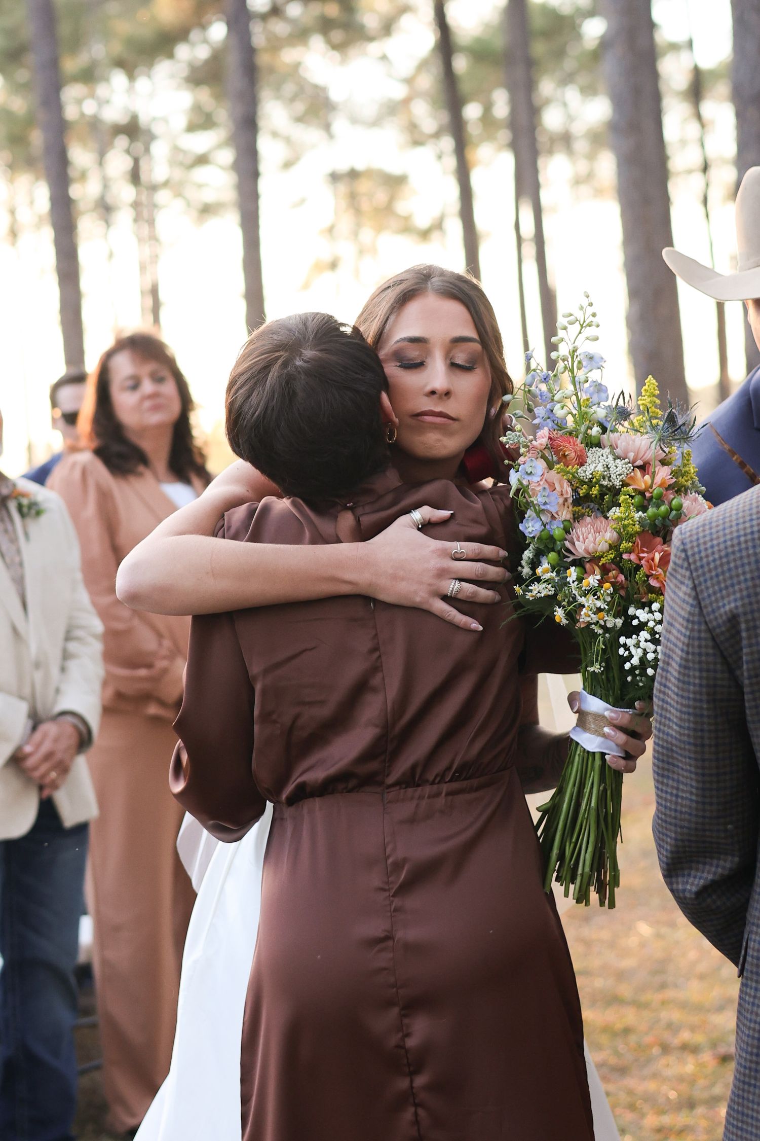 Emotional embraces shared between wedding party members in brown dresses during outdoor celebrations.