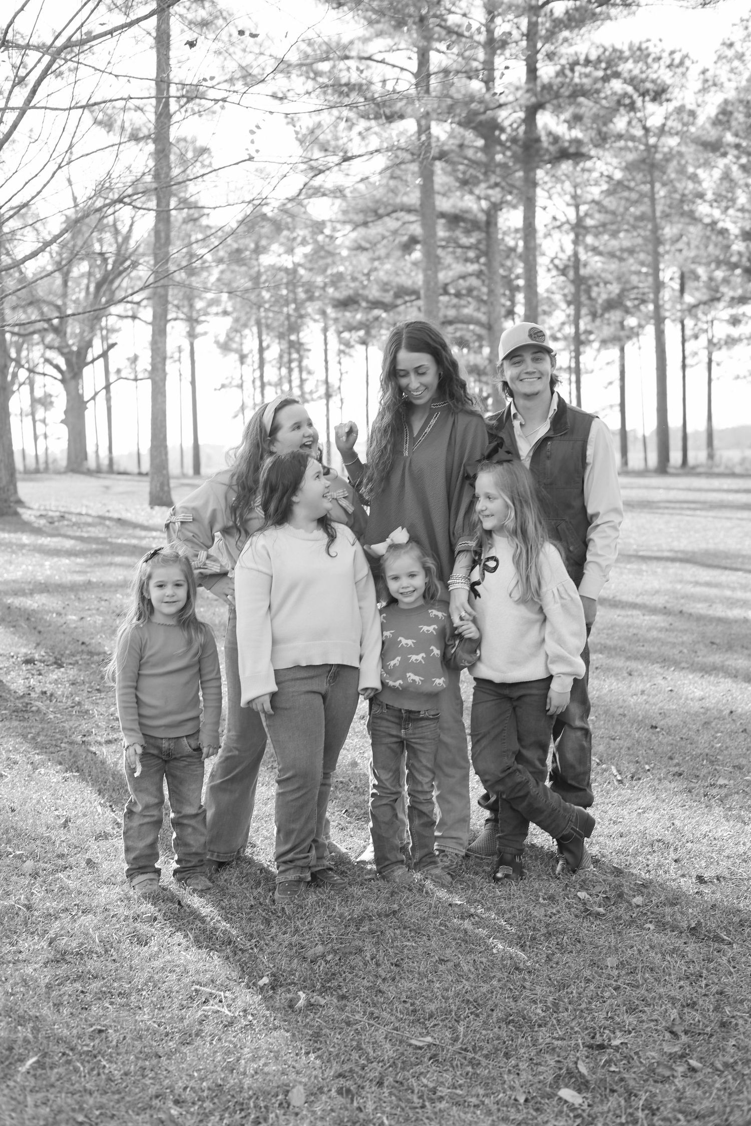 A group of people walking together on a grassy hill among tall pine trees in black and white.