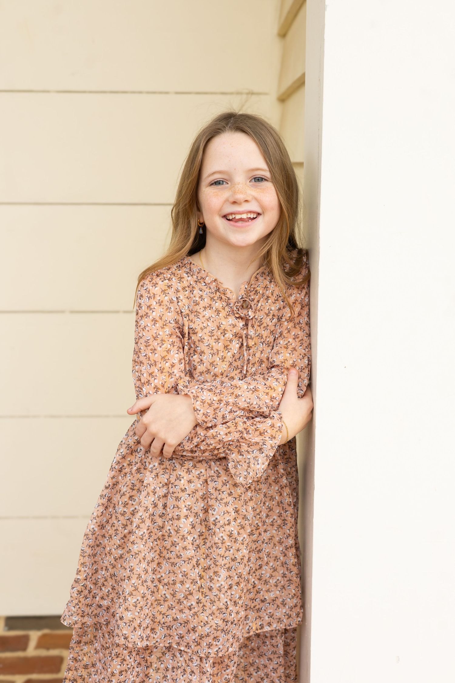 A young child in a floral print dress smiles and poses playfully in a series of three connected photos.