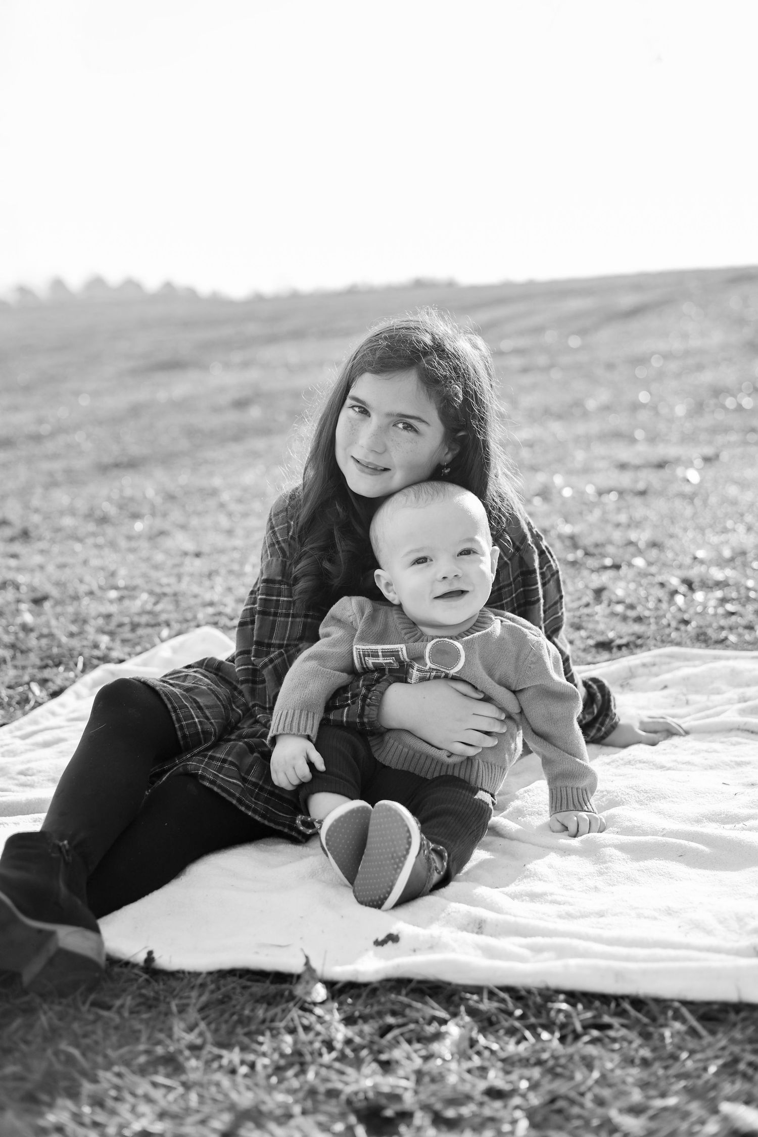 A black and white photo series shows a parent and baby lying on a blanket outdoors in casual poses.