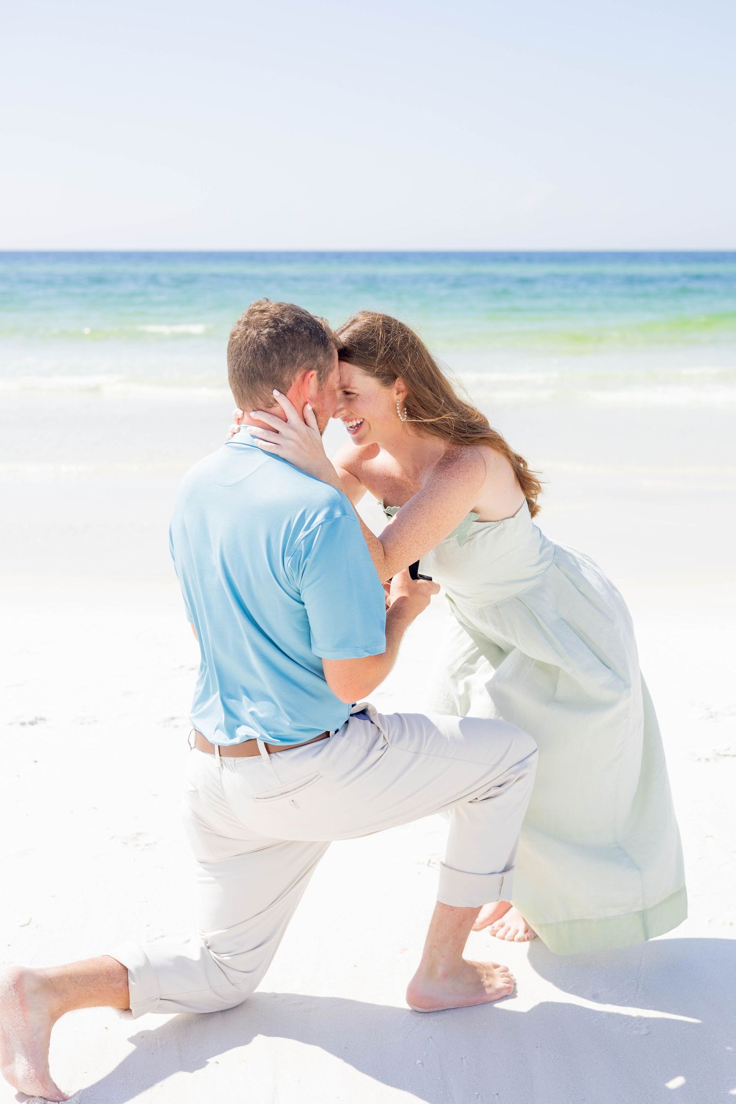 Man down on one knee proposing to his girlfriend on a beautiful sunny white sand beach.