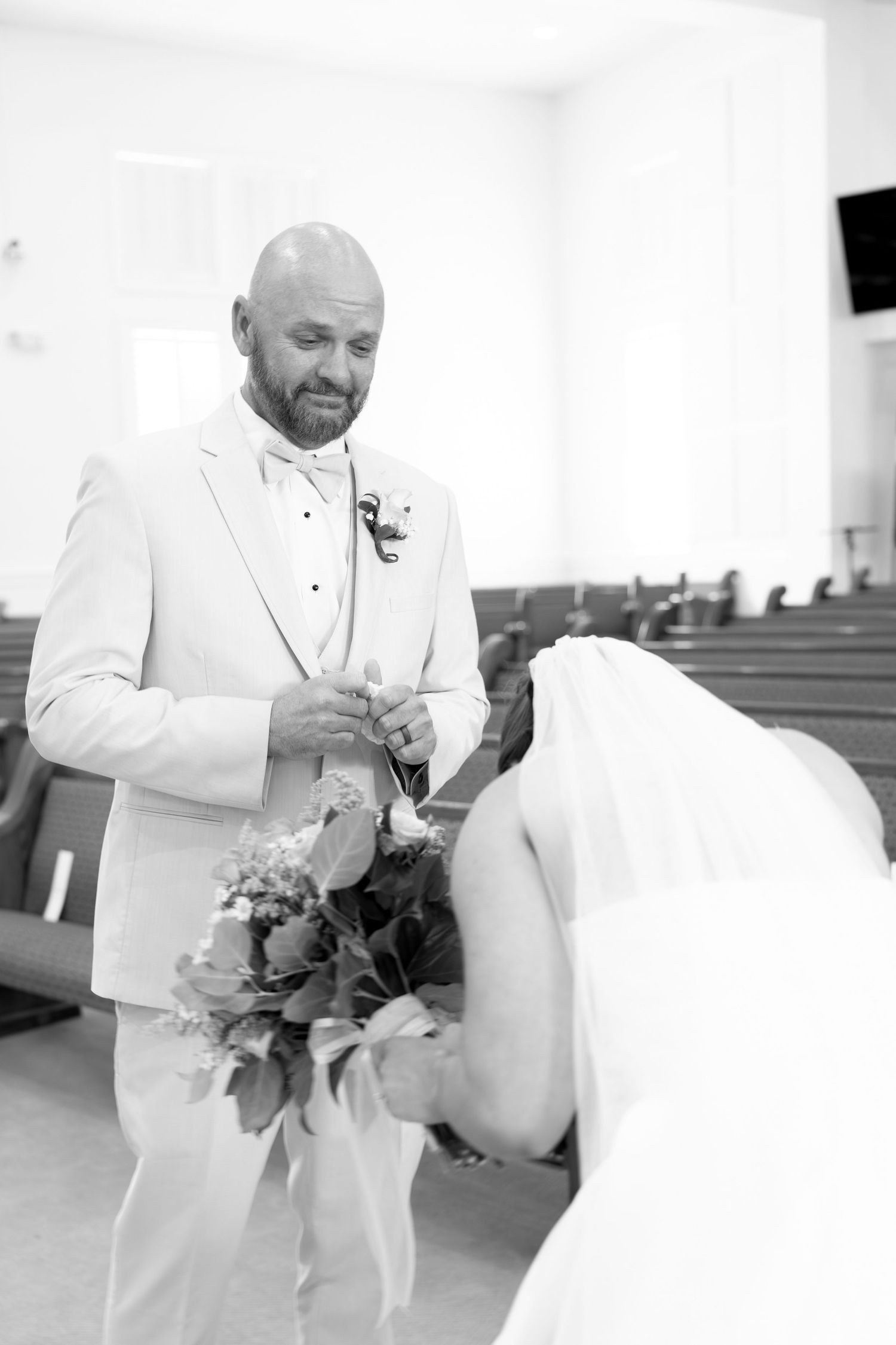 Black and white photo of bald groom exchanging rings with bride during church wedding ceremony.