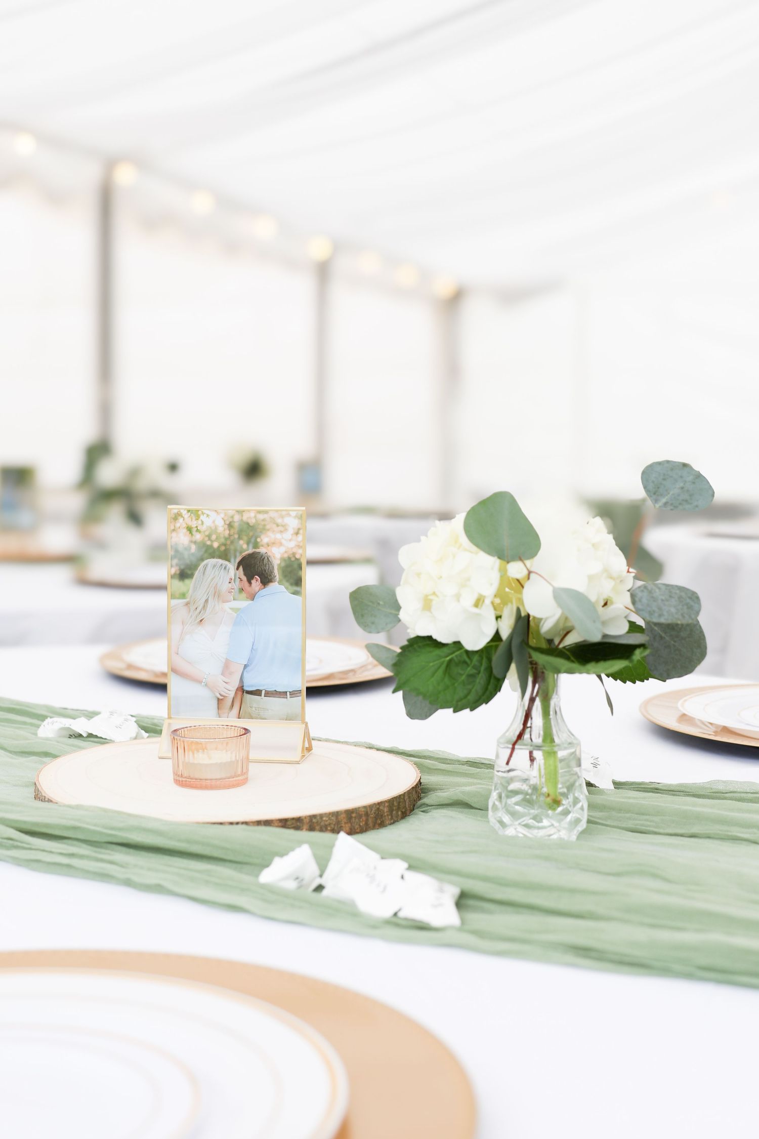 Elegant wedding reception table with sage green runner, white hydrangeas, and couple photo centerpiece.
