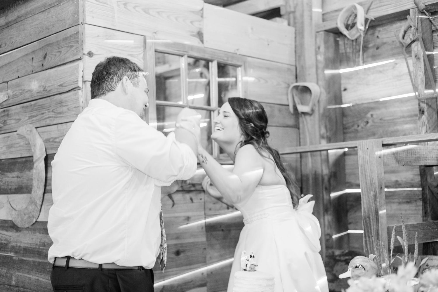 Black and white photo of a bride and groom sharing a first dance outside a rustic wooden barn venue.