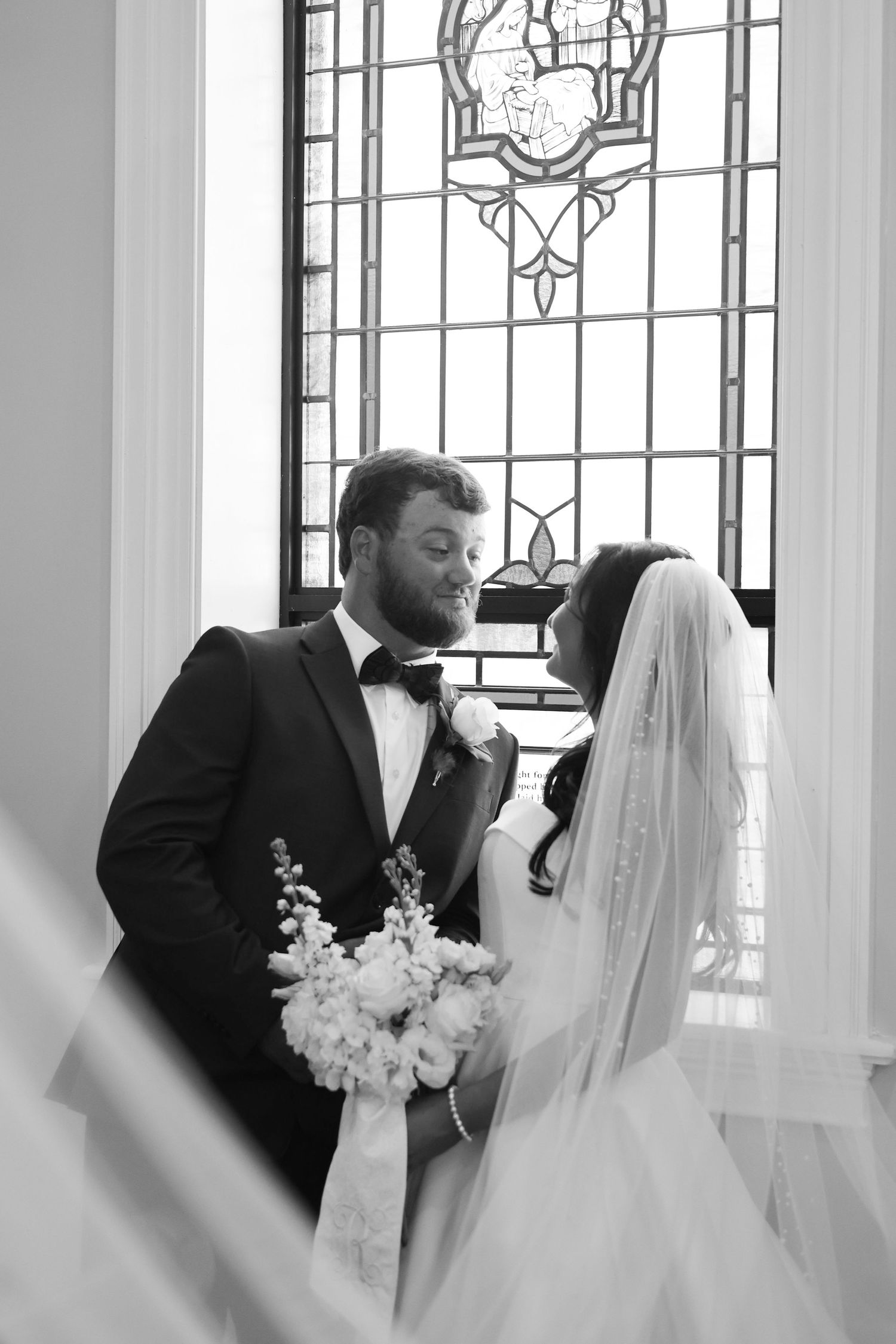 Black and white wedding photos in front of stained glass windows showing an intimate moment.