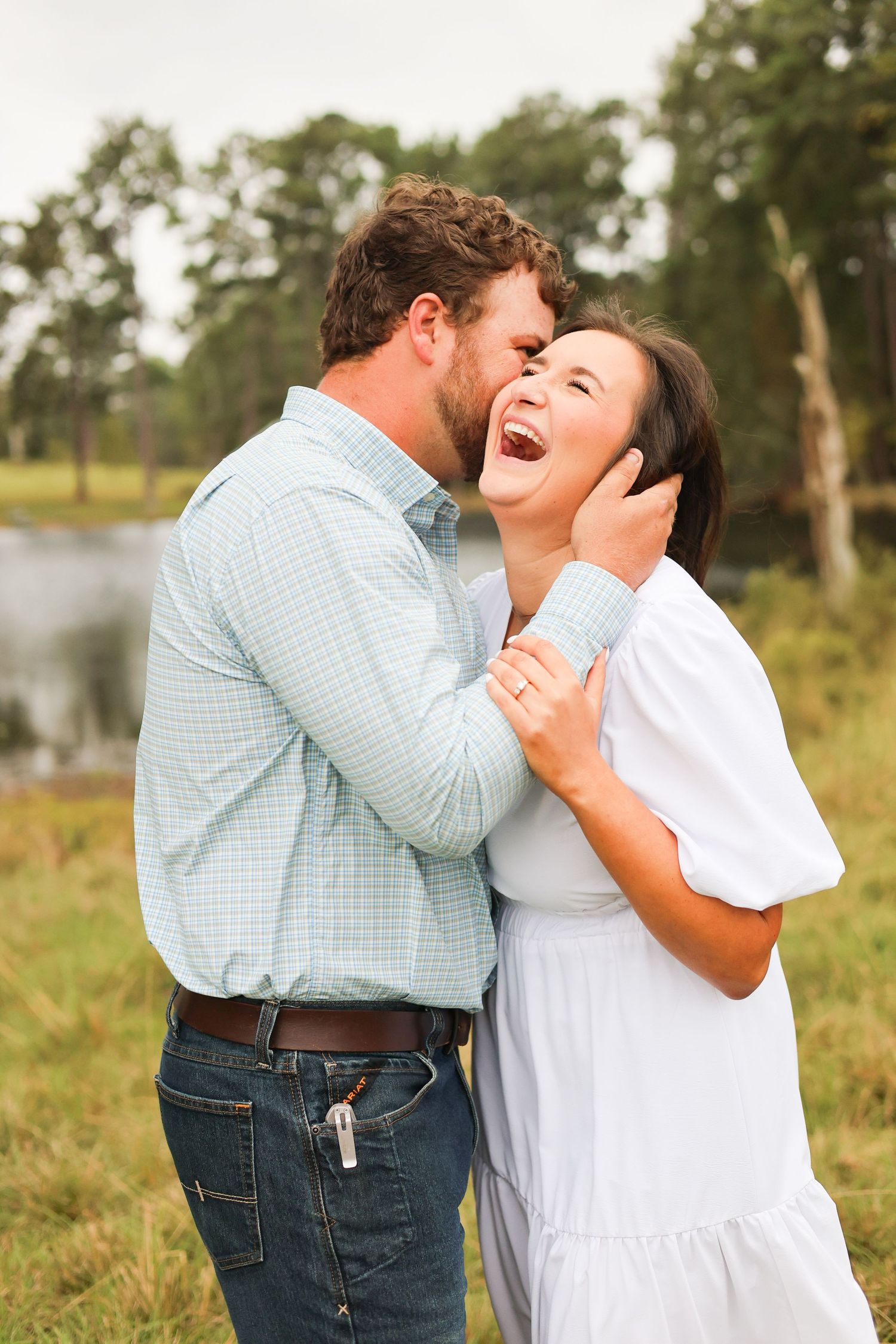 A joyful couple sharing a candid laughing moment outdoors by a lake.