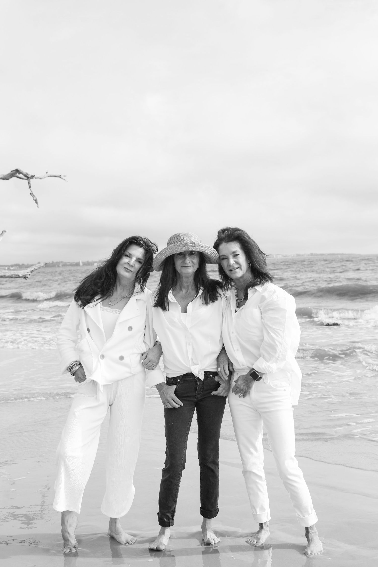 A group in white outfits poses playfully together on a beach in black and white photography.