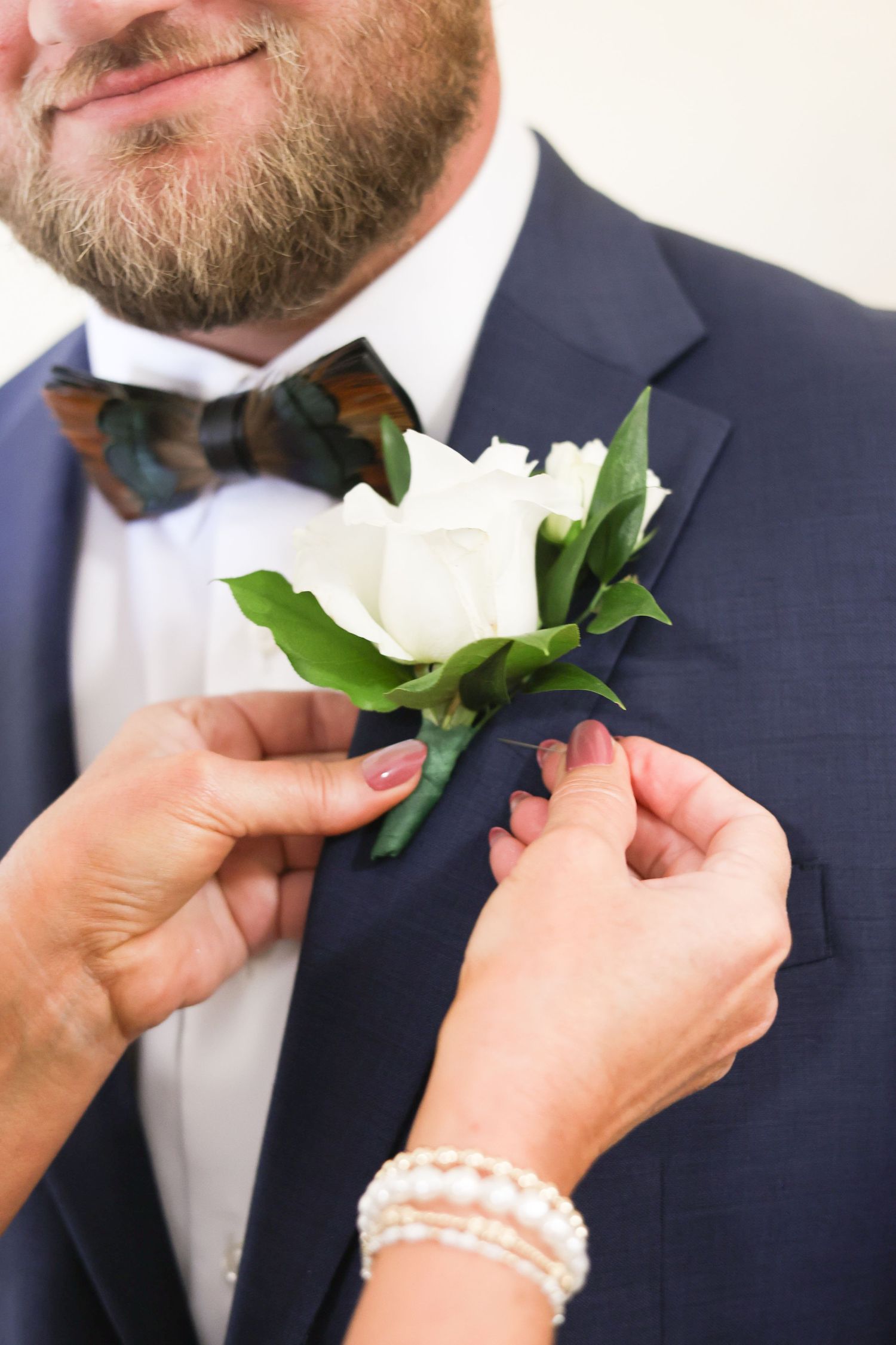 Hands pinning a white boutonniere flower onto a navy suit jacket.