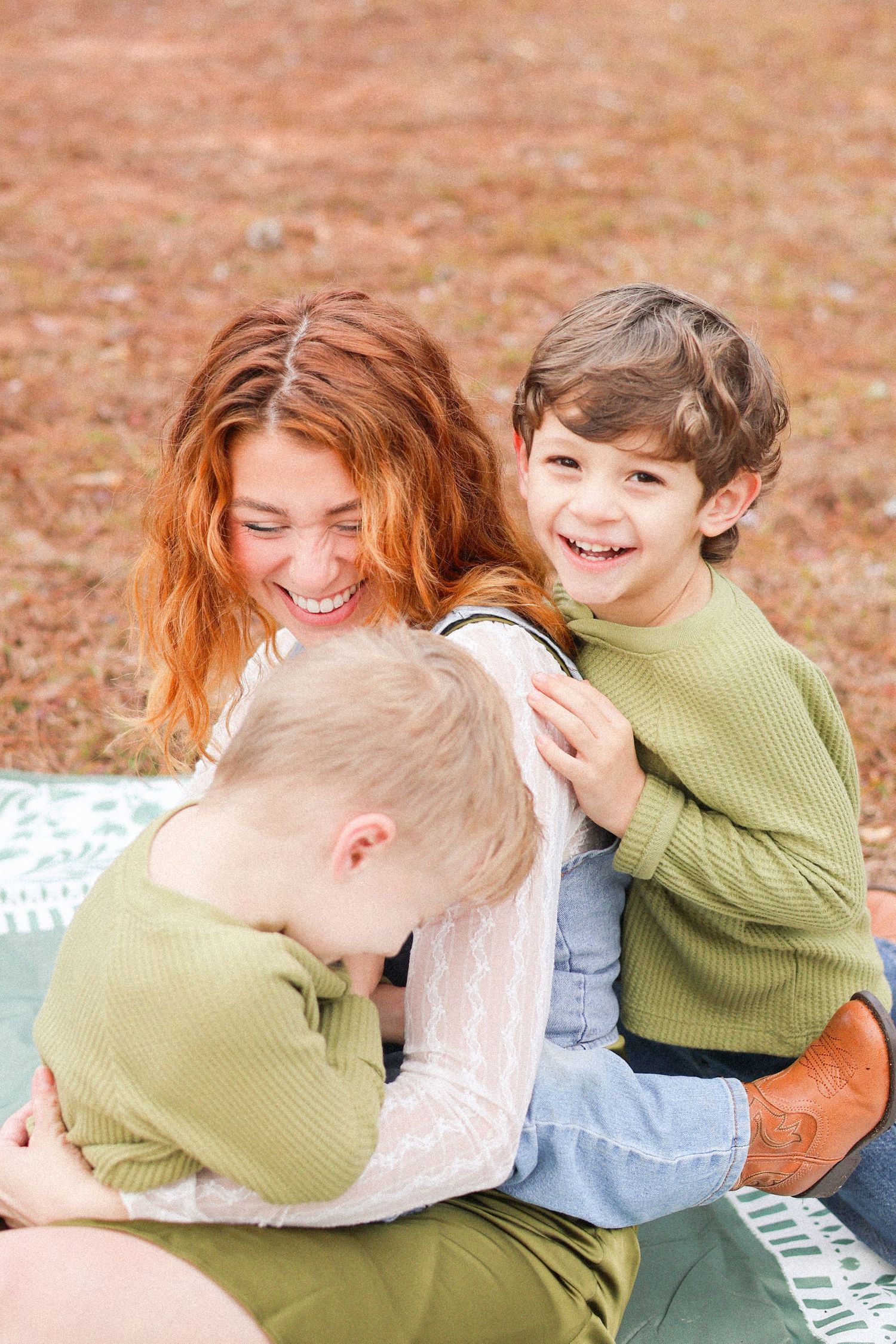 A joyful family moment captured outdoors on a blanket, wearing matching green sweaters and sharing laughter together.