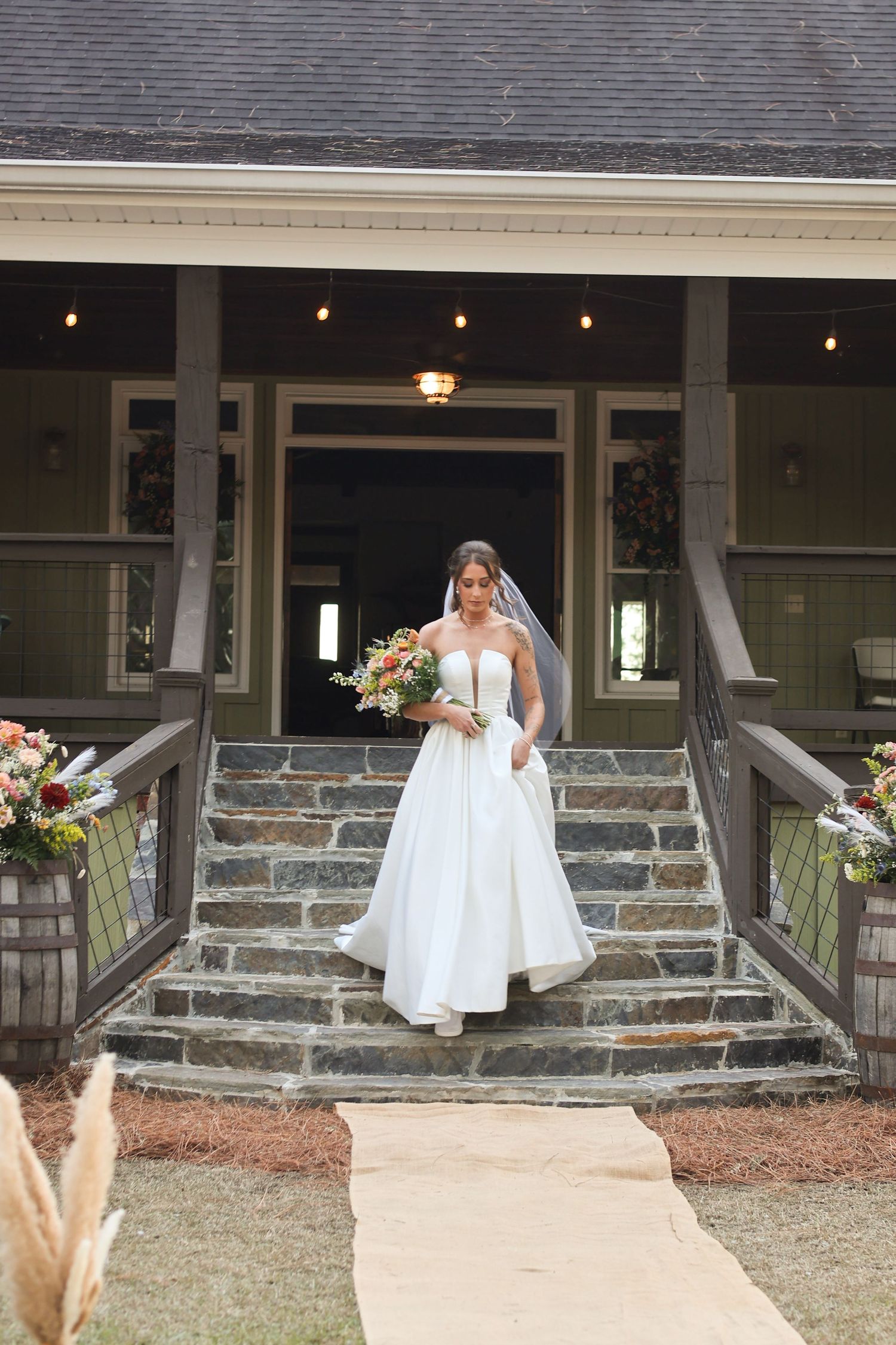 A bride descends stone steps outside a rustic wedding venue decorated with string lights.