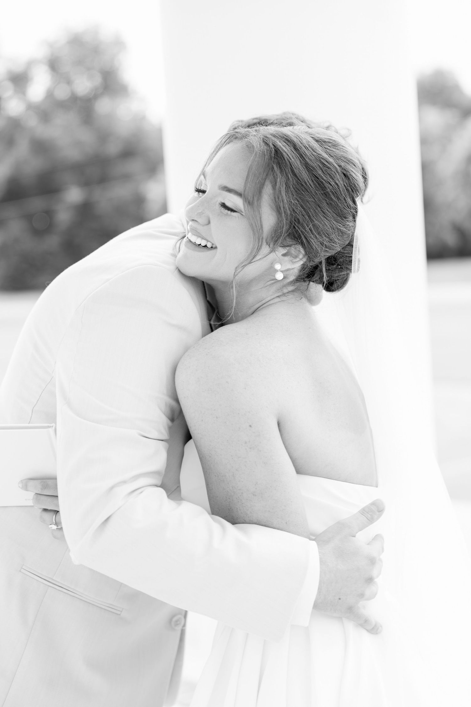Joyful bride embracing groom in black and white wedding portrait near columns.