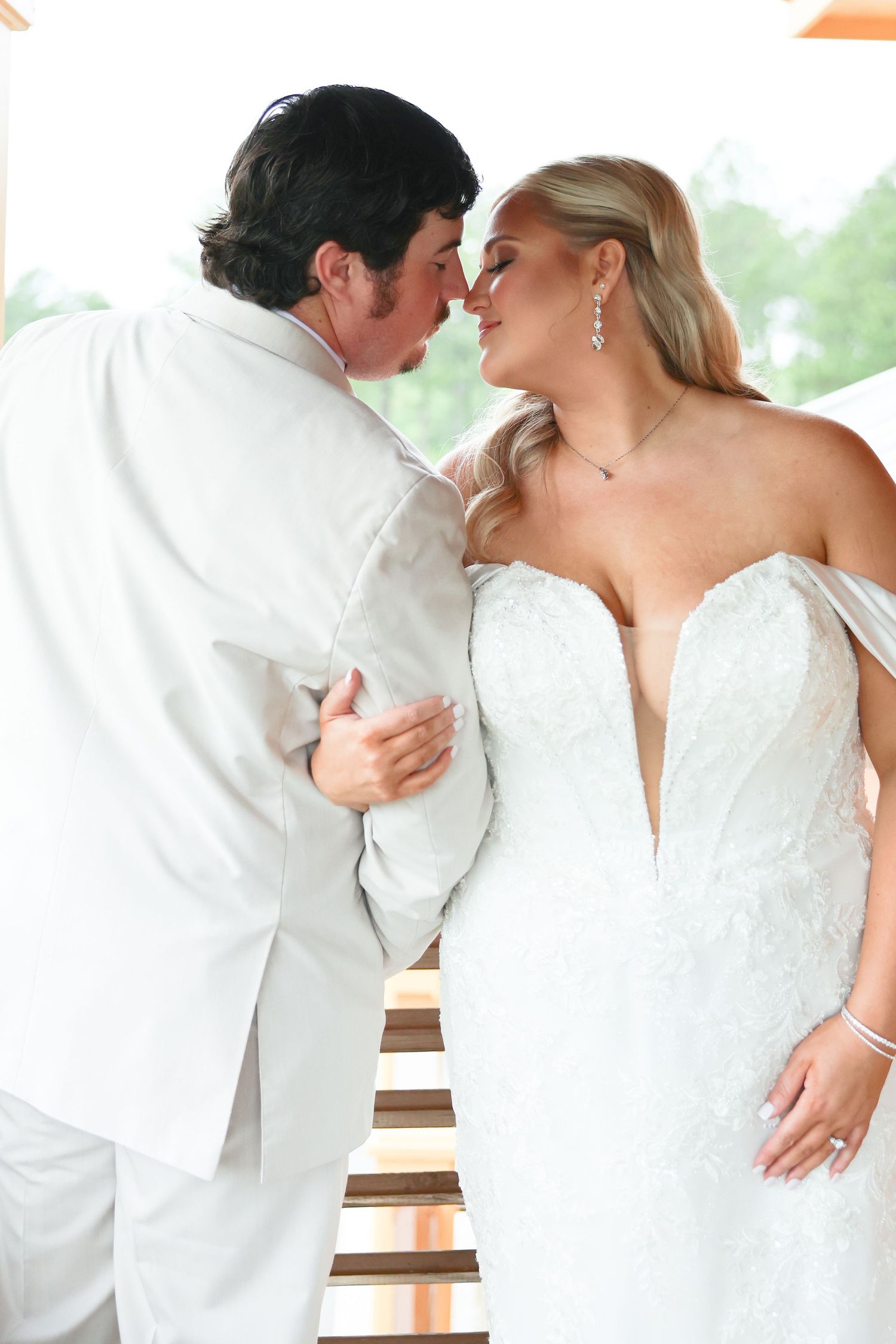 Bride and groom sharing intimate almost-kiss moment, bride in deep V-neck lace wedding gown.