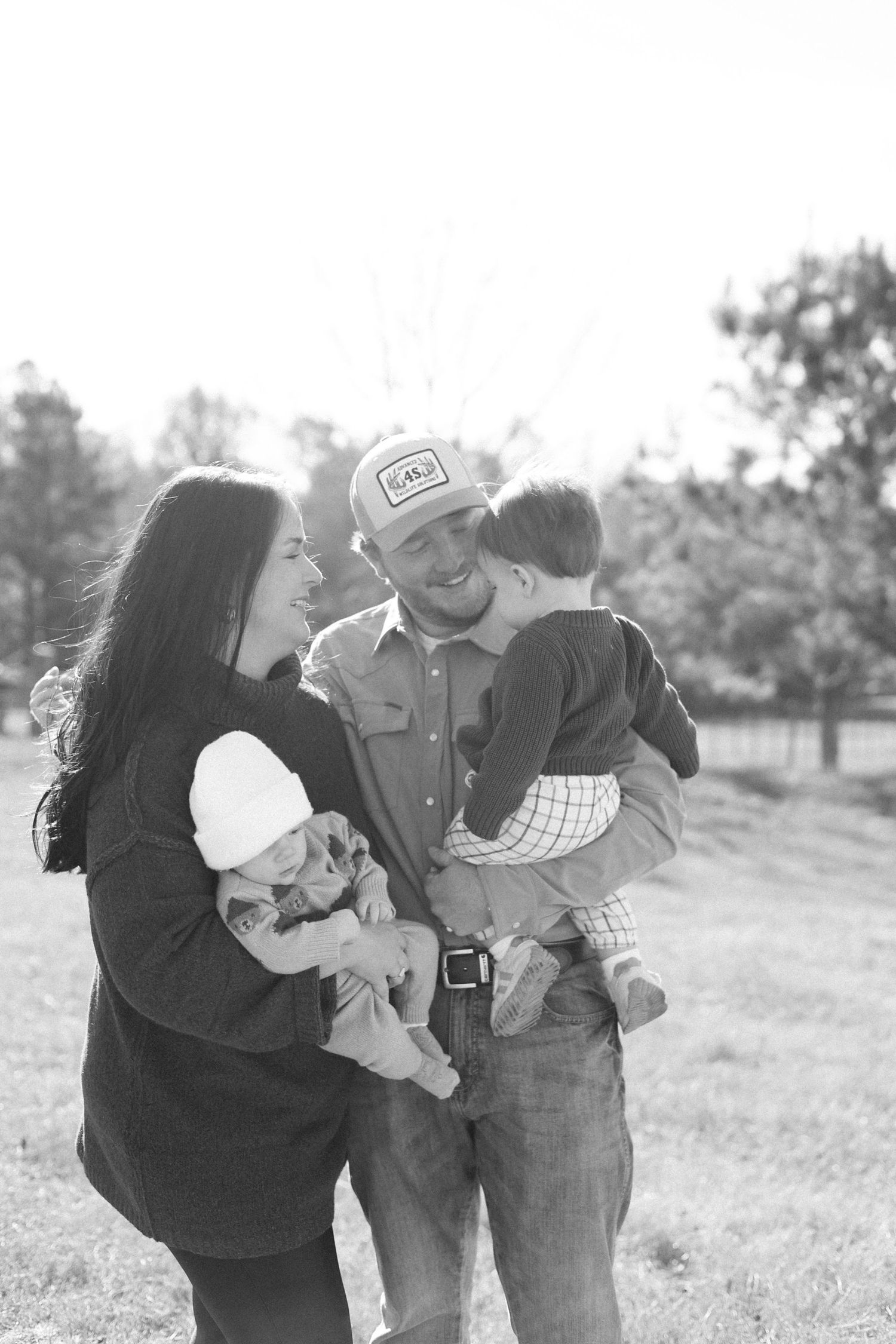 A series of black and white photos showing a couple embracing in a field with trees in the background.