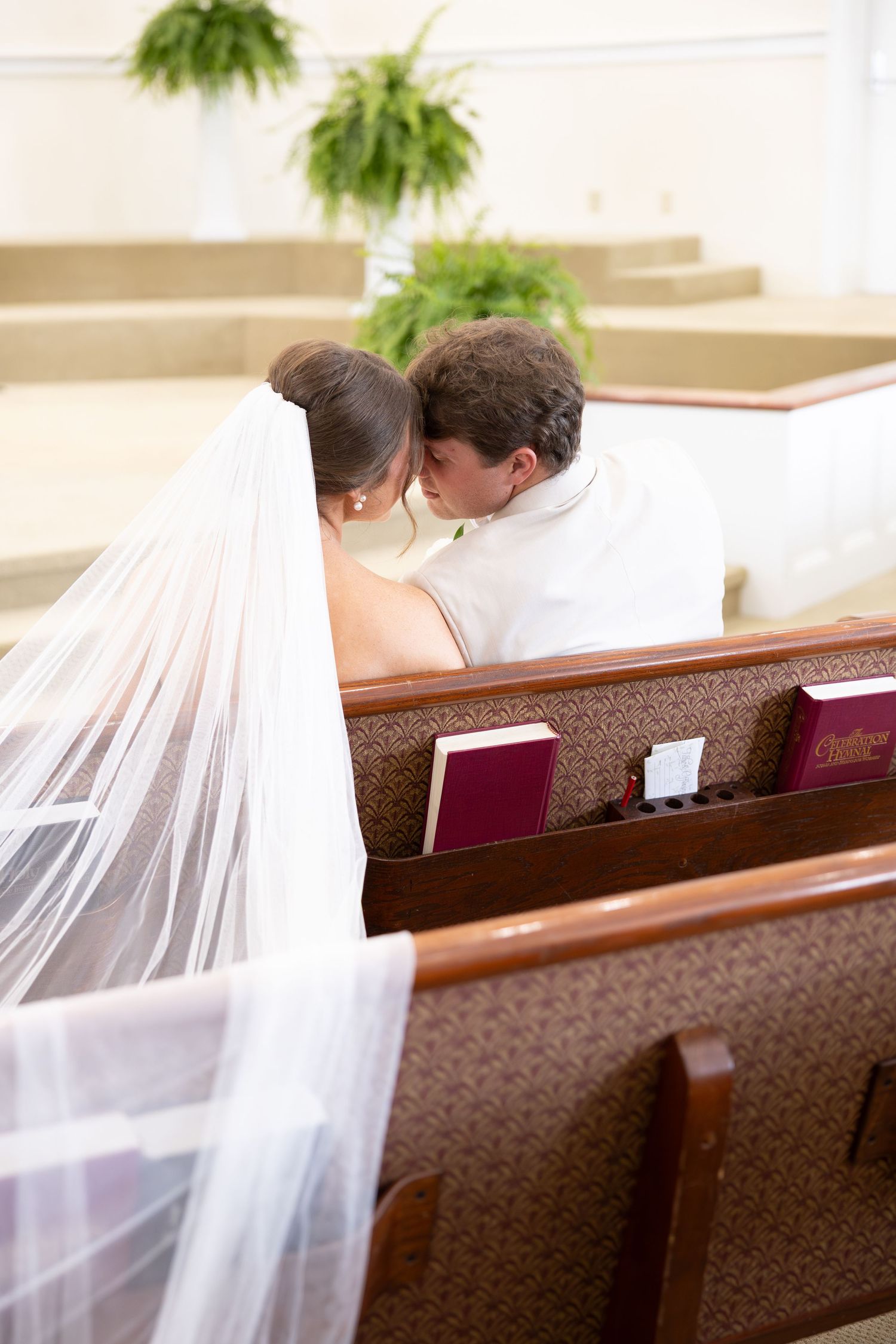 Bride and groom share intimate kiss in church pew during wedding ceremony.