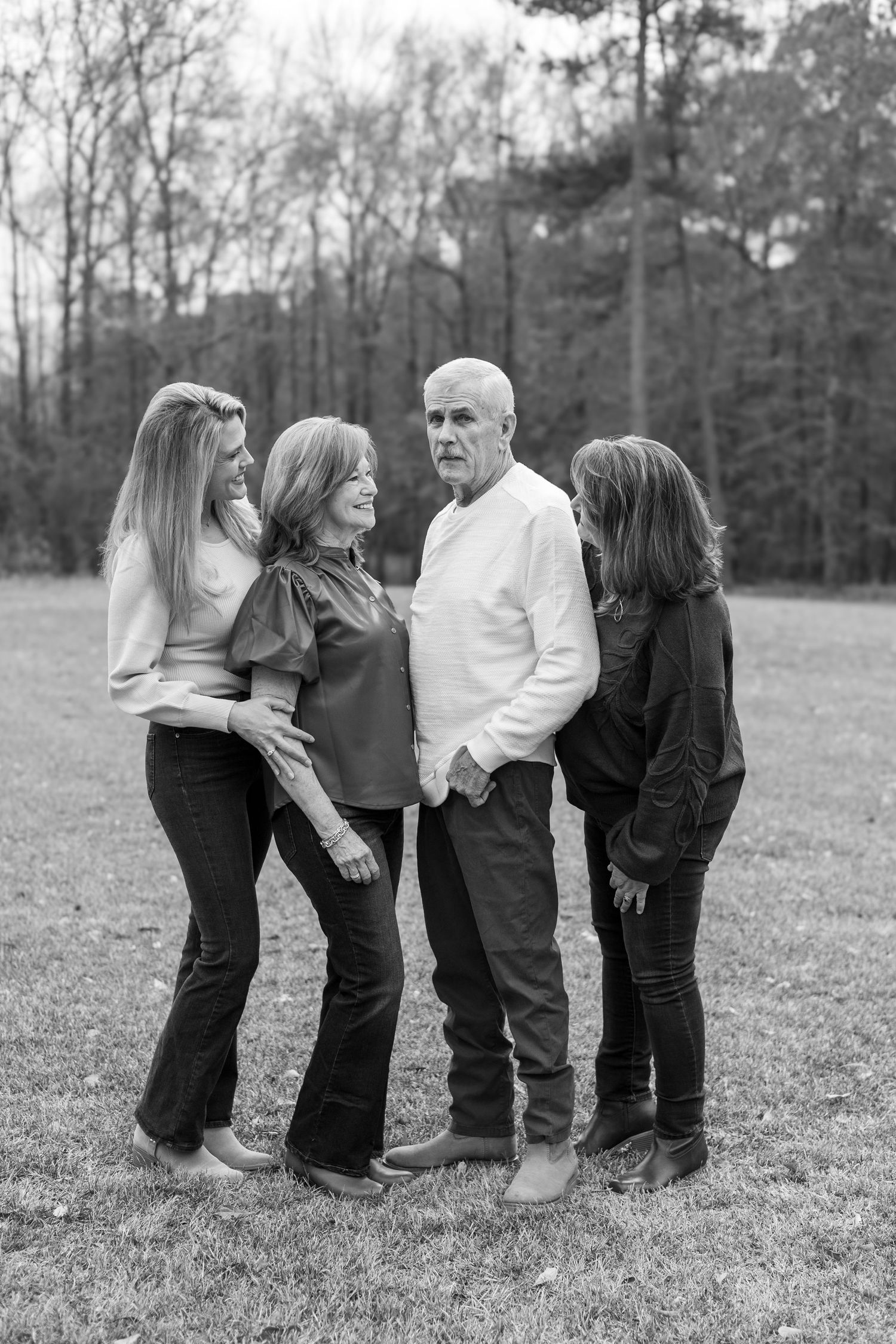 A black and white portrait of a family group standing together outdoors in a natural wooded setting.