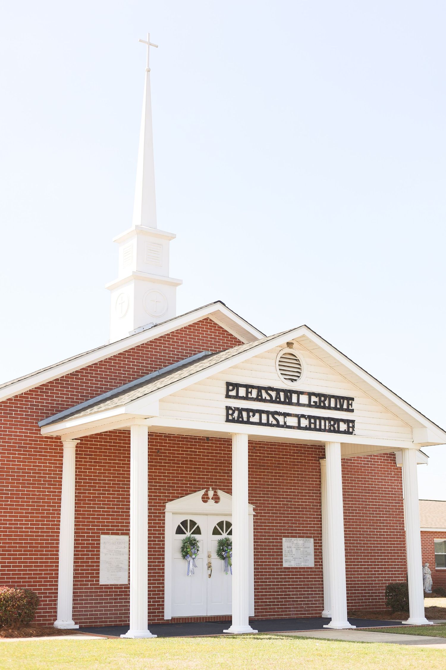 Red brick Baptist church with white columns and steeple against a blue sky.