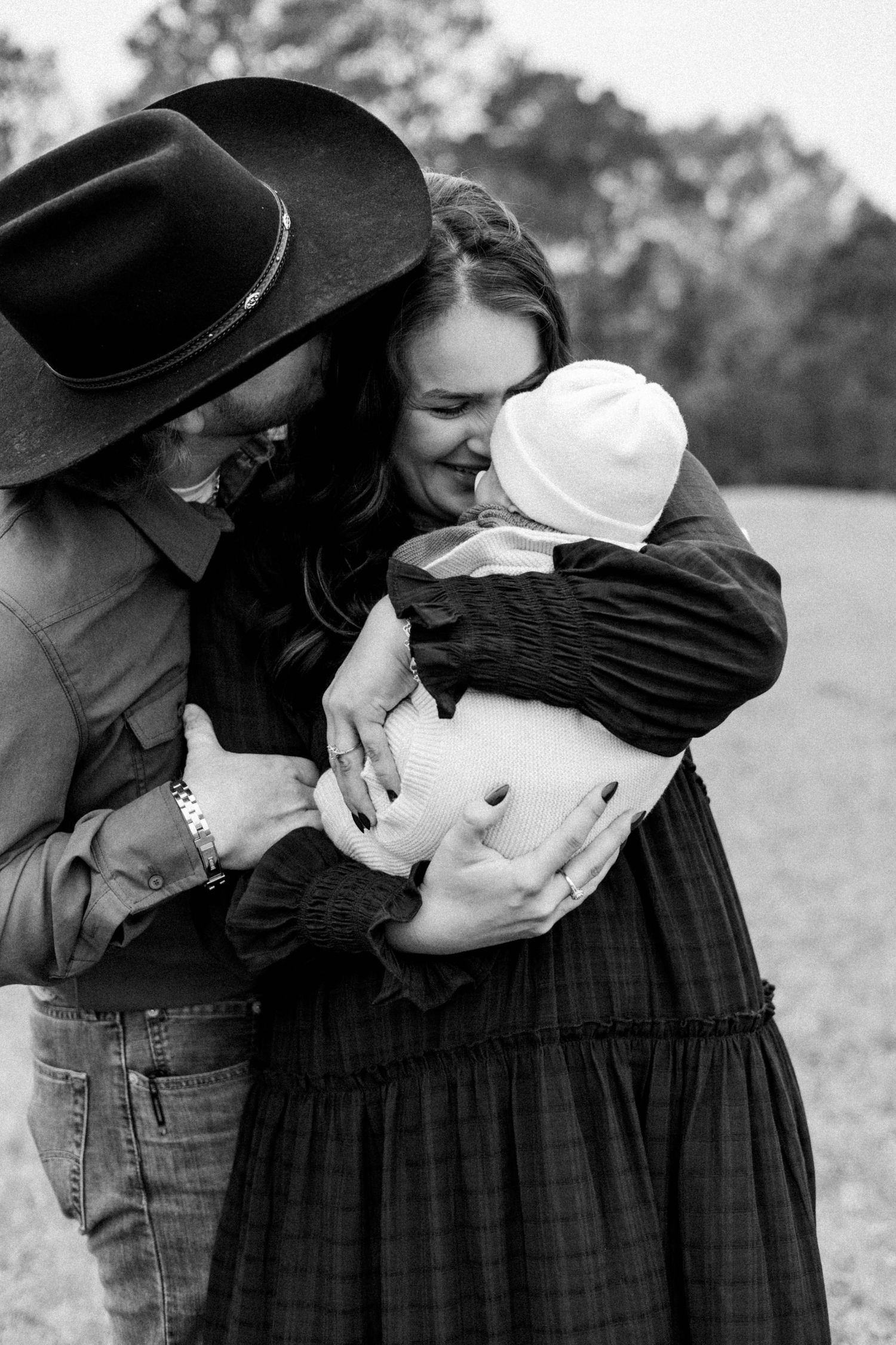 Parents sharing intimate moments with their newborn baby in a rustic outdoor setting.