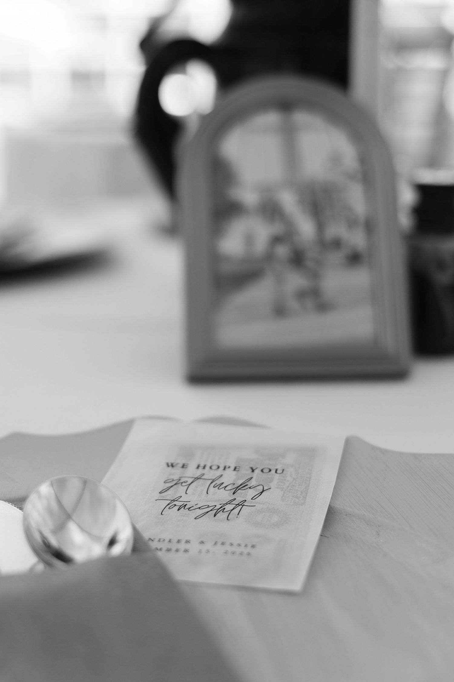 A black and white wedding invitation card with elegant calligraphy text sits on a table.