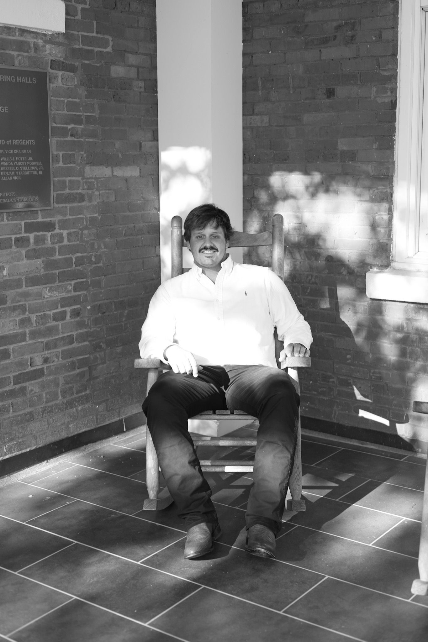 Graduate in academic dress relaxing on tiled floor between brick walls.