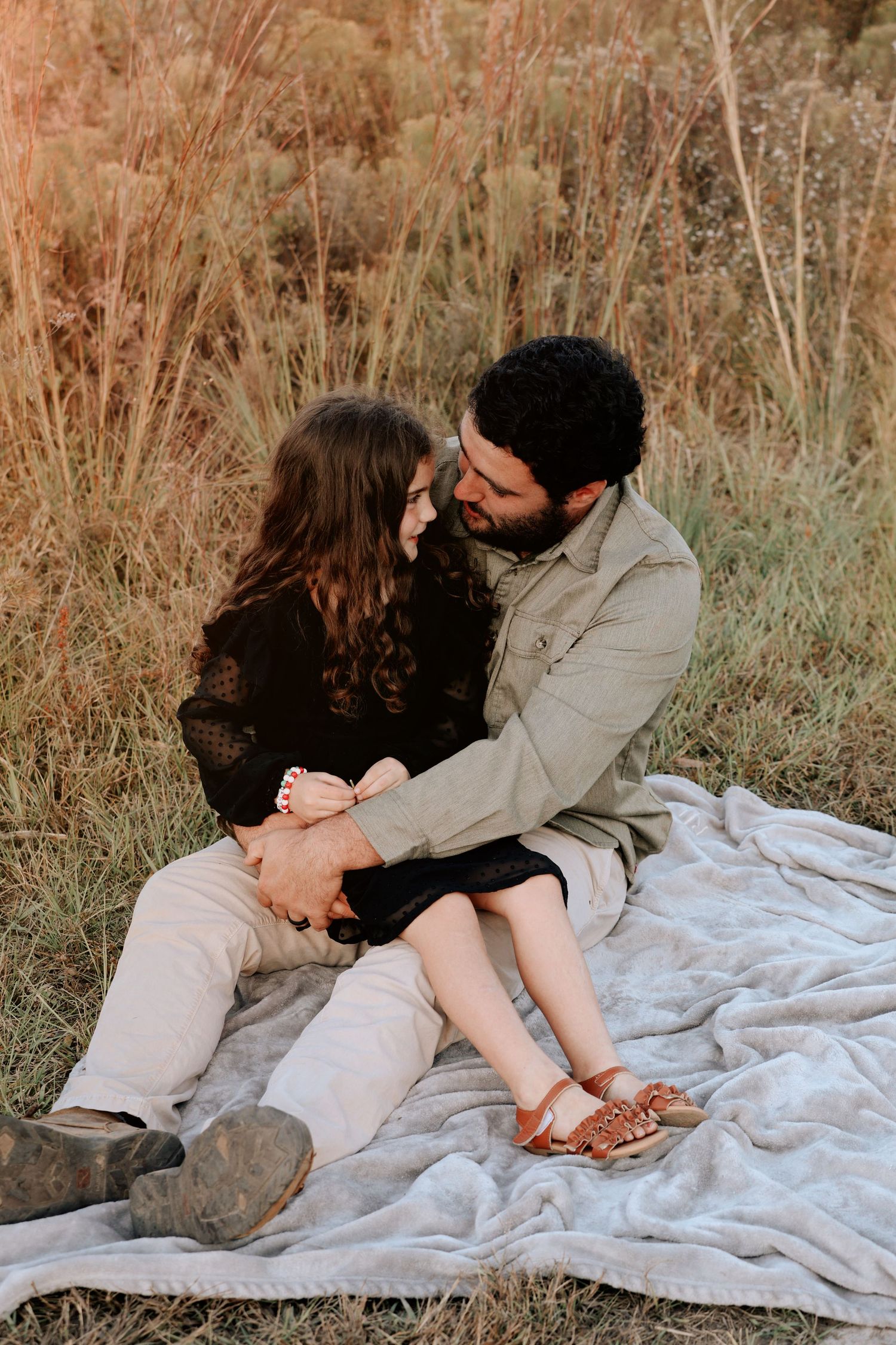 Couple sitting on a blanket in a field, gazing at each other romantically during golden hour.