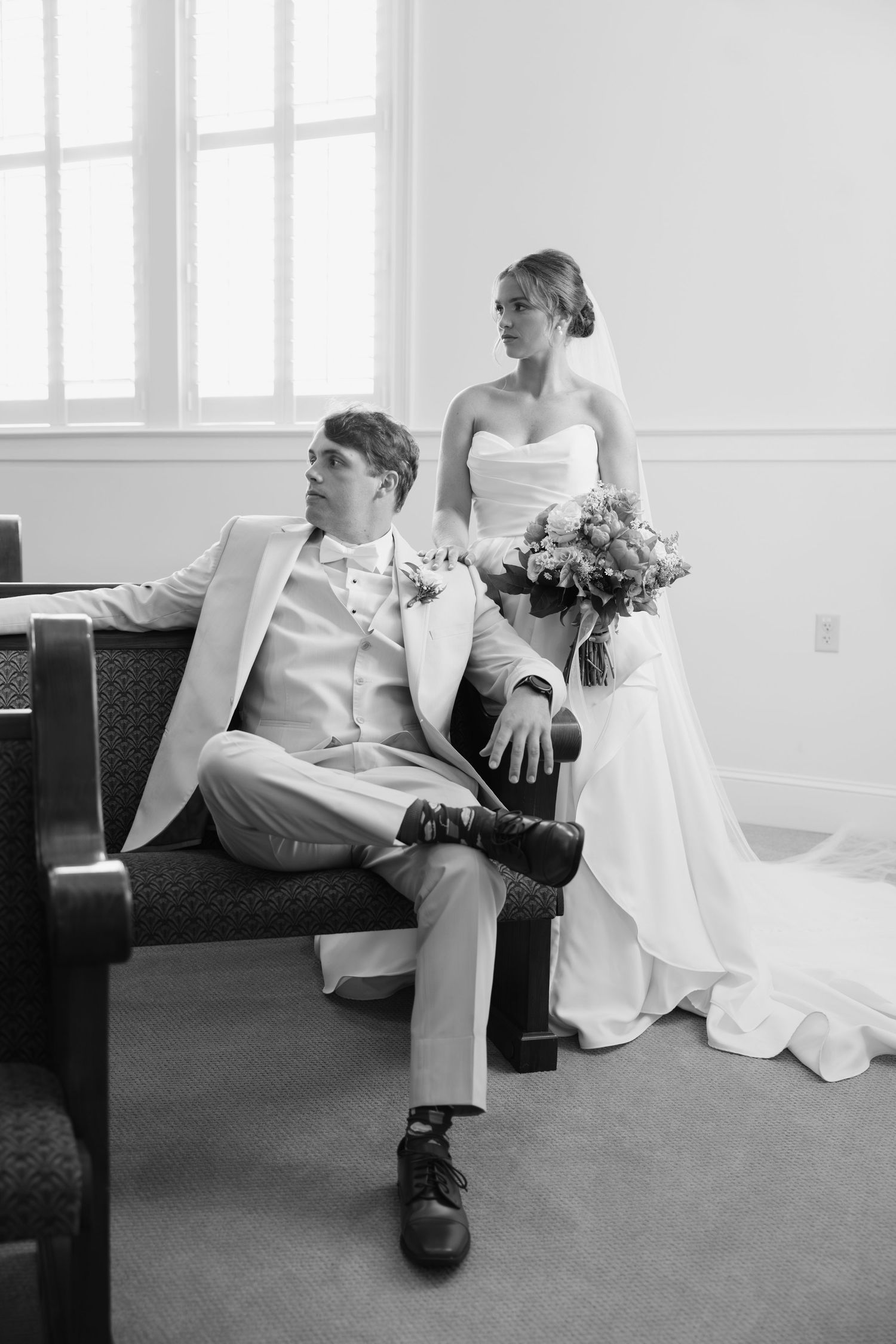 Black and white photo of bride and groom sitting in church pew with bouquet.