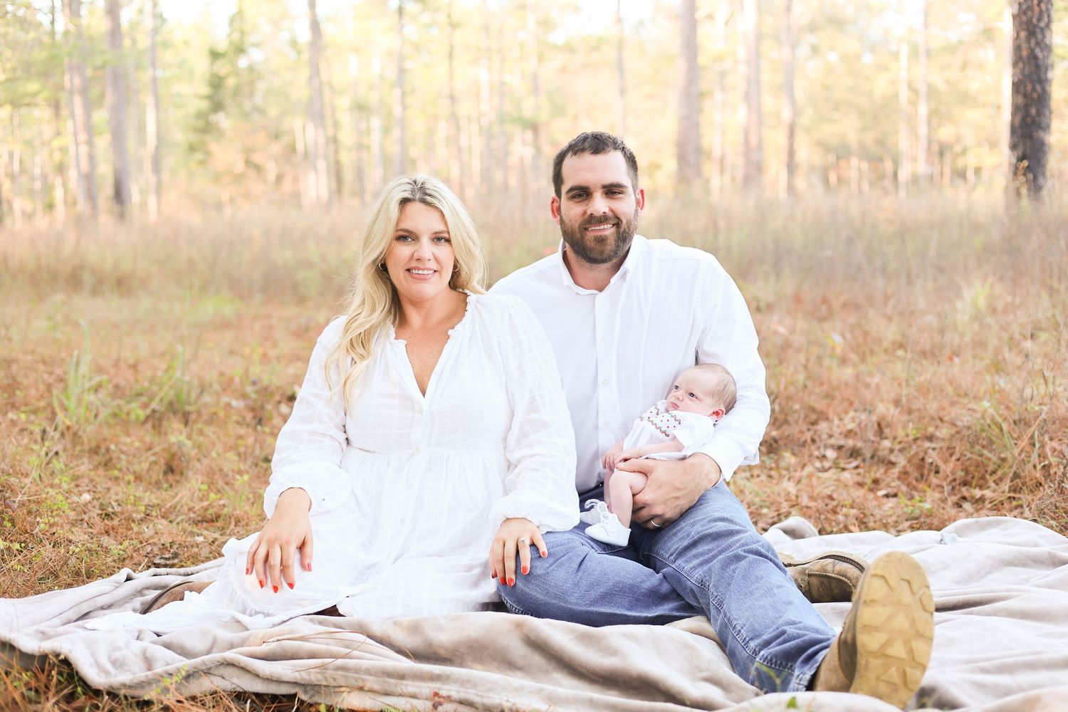 A couple in white clothing relaxes on a blanket in a golden field during an outdoor autumn photoshoot.