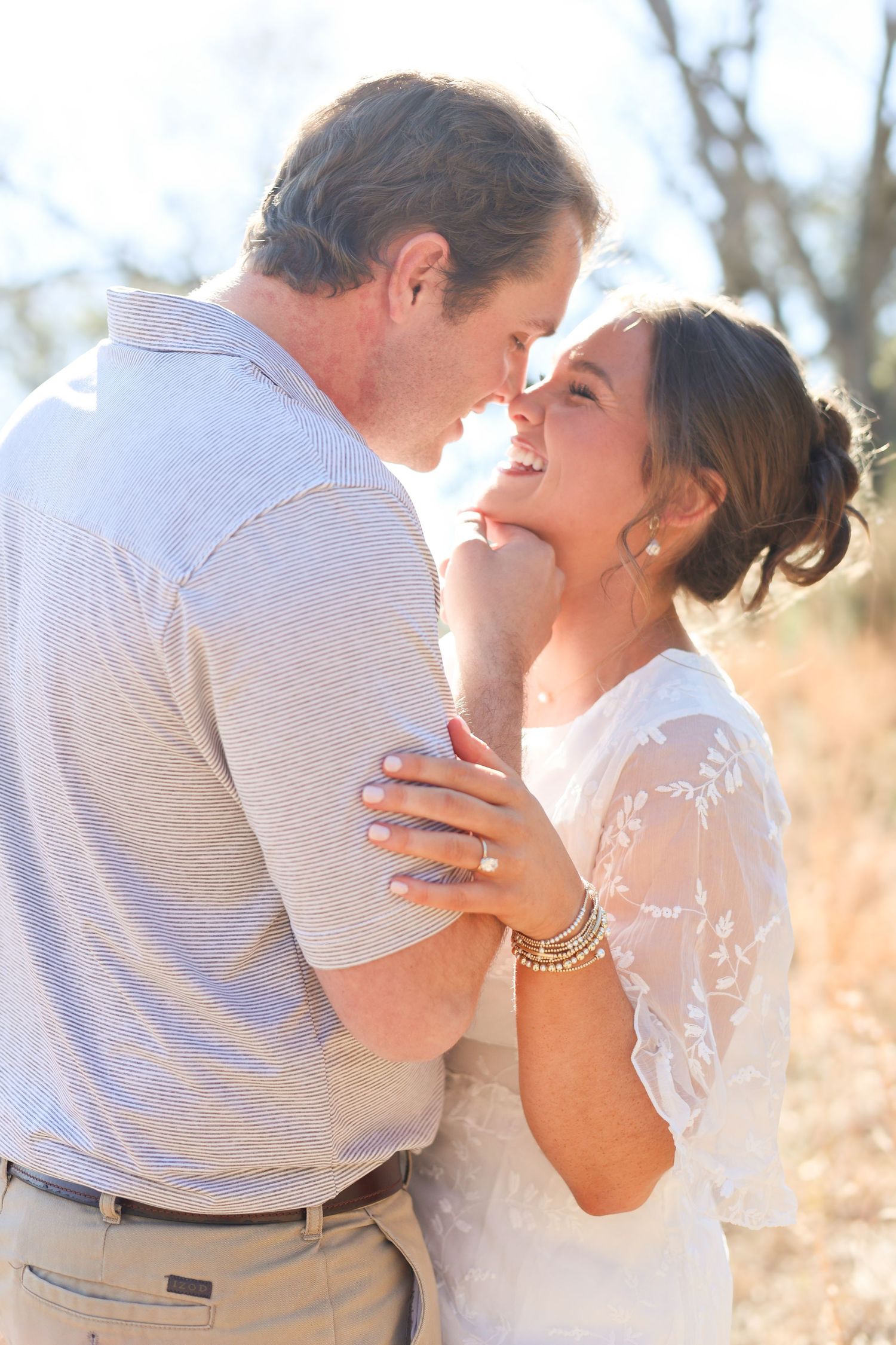 A romantic couple embraces in a sun-drenched field during a golden hour photoshoot.