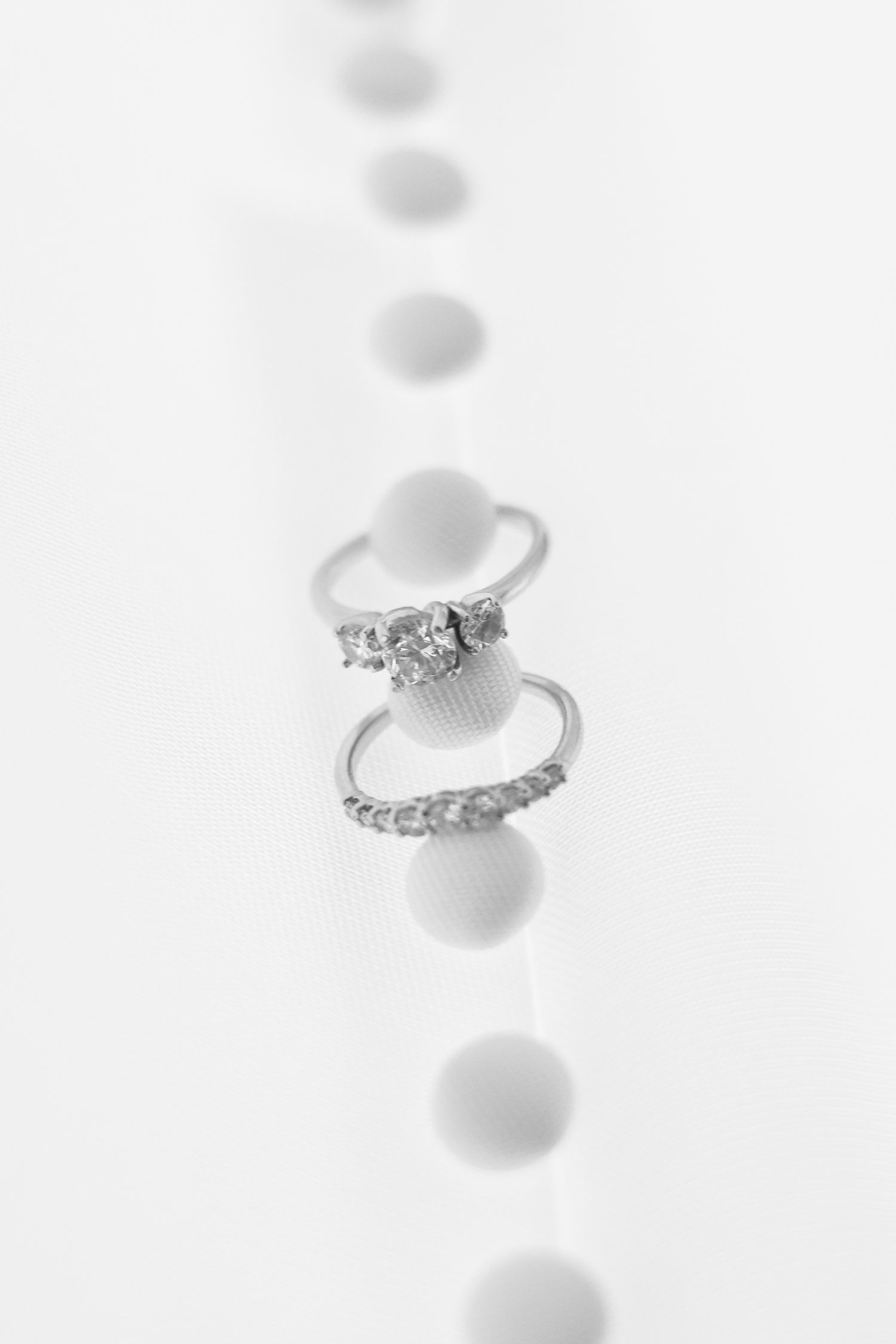 Two silver diamond rings stacked together on a white surface with bokeh dot pattern background.