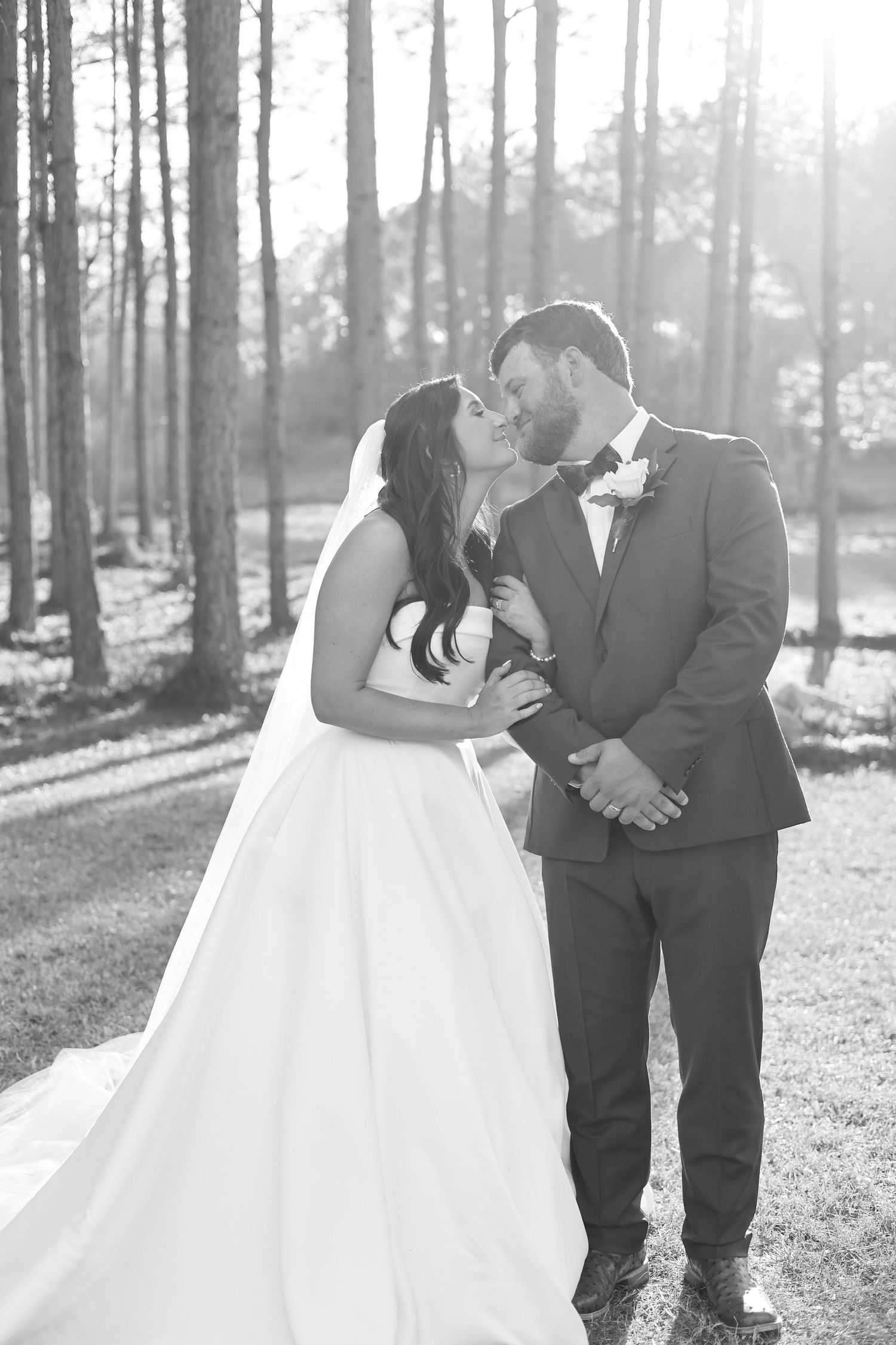 A romantic black and white wedding photo series showing a couple embracing among tall trees in a sunlit forest.