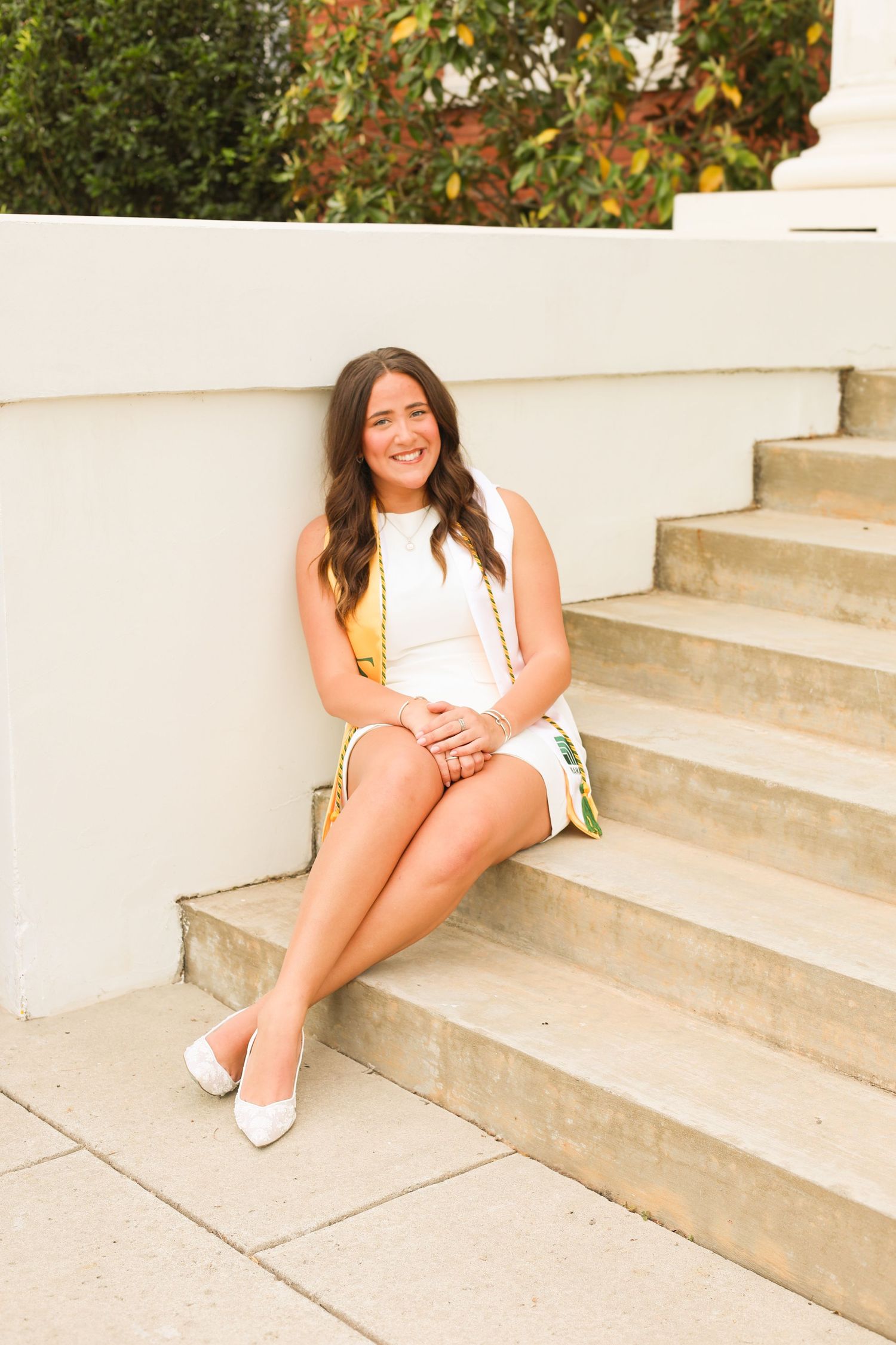 Graduate poses on white stone steps during outdoor photo session.