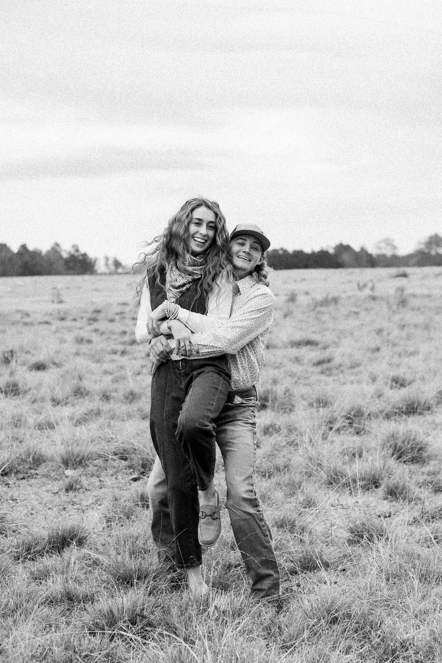 Black and white photo of couple playfully posing in open field.