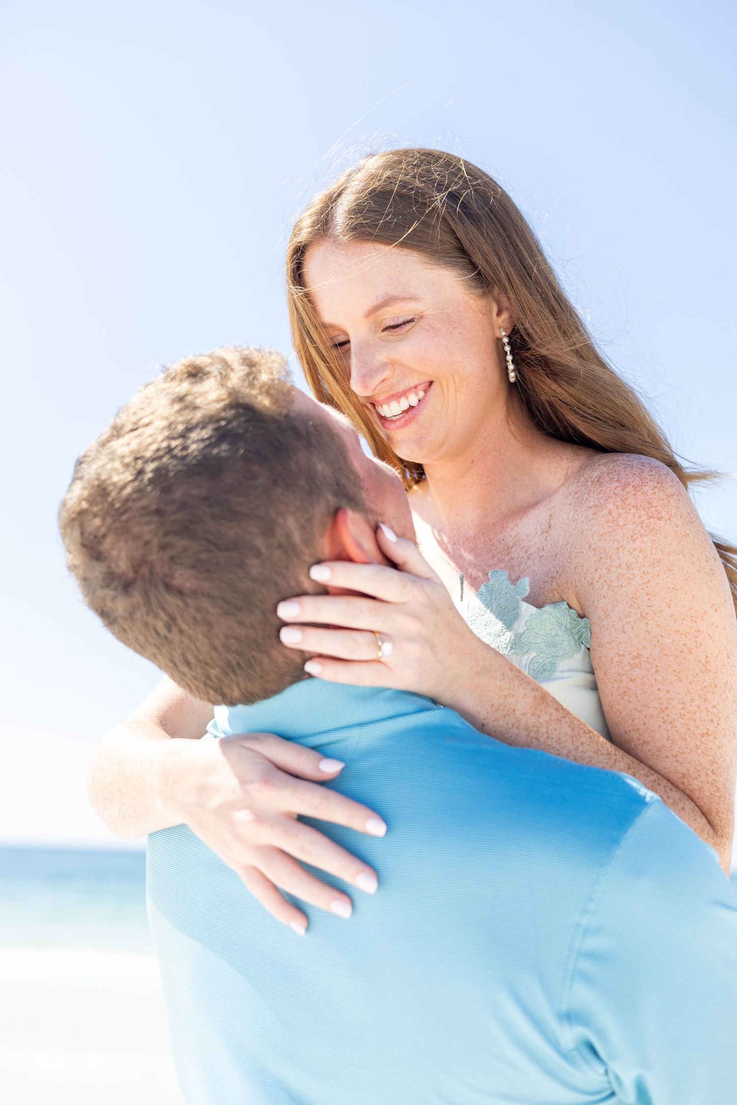 A joyful embrace captured on a sunny beach with ocean waves in the background.