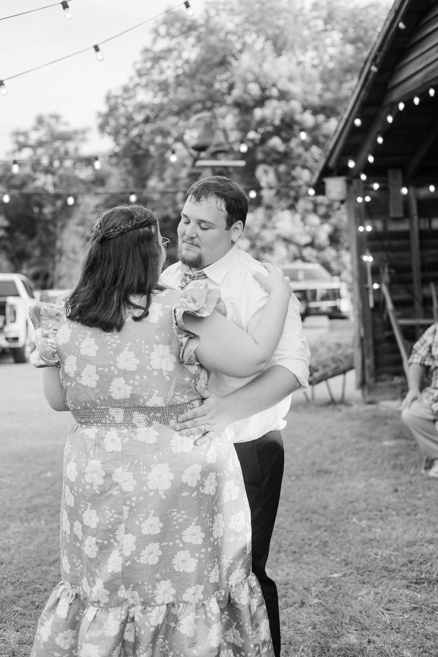 Couple sharing an intimate first dance outdoors at a rustic barn wedding reception under string lights.
