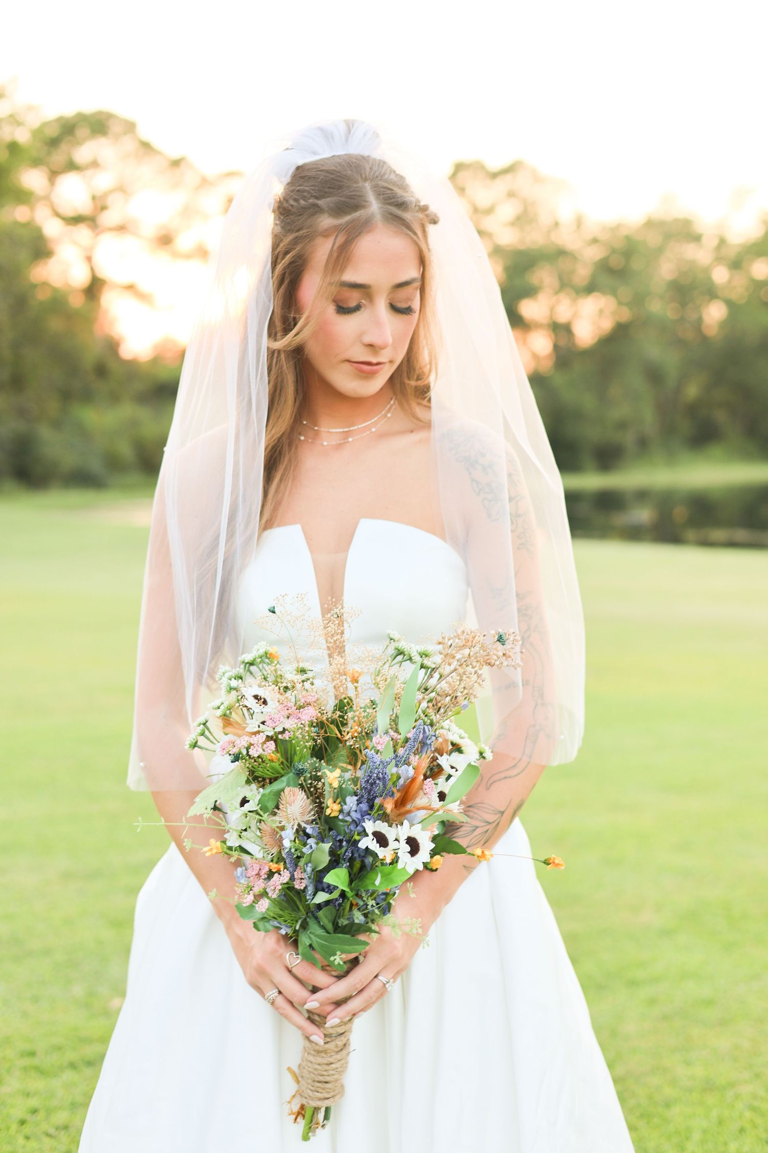 Bride holding colorful wildflower bouquet featuring blue and white flowers in outdoor garden setting.