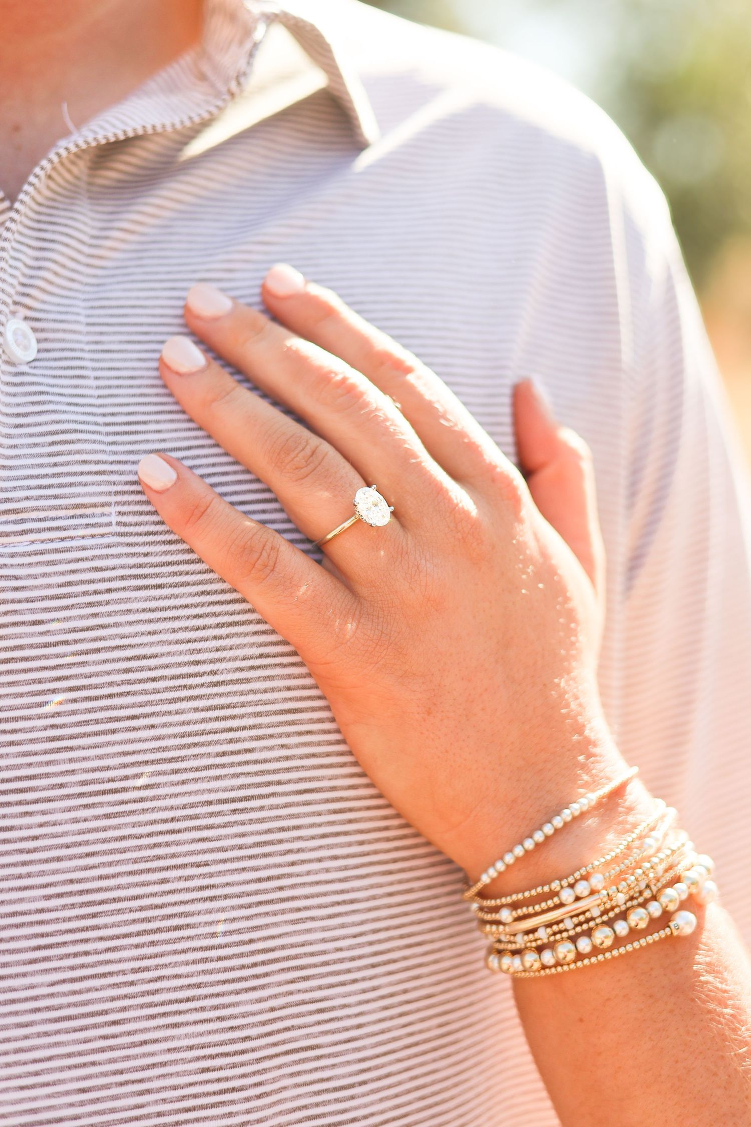 Close-up view of a hand wearing a diamond engagement ring and multiple delicate pearl and gold stacked bracelets.