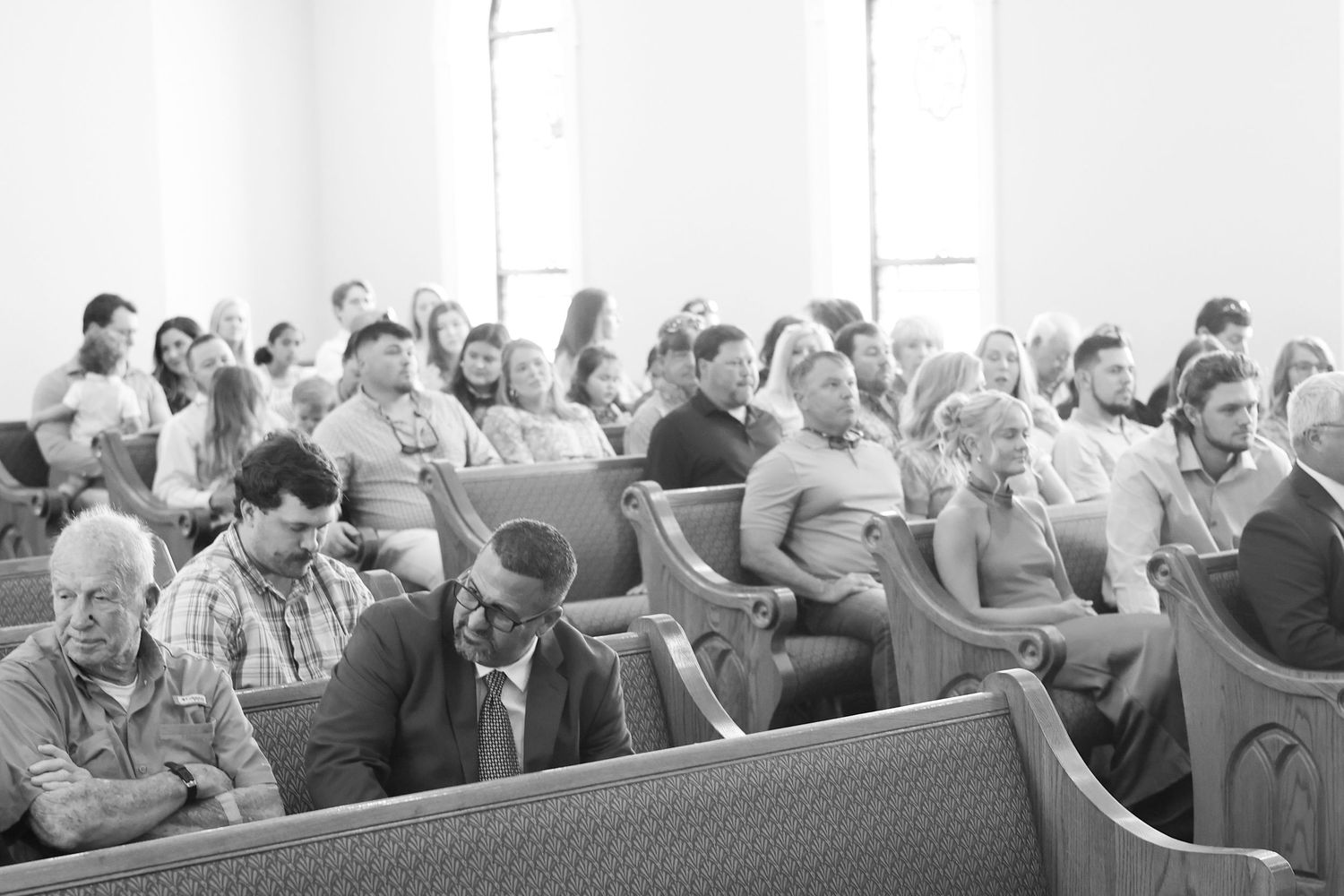 Black and white photo of a congregation seated in wooden church pews during a religious service or ceremony.