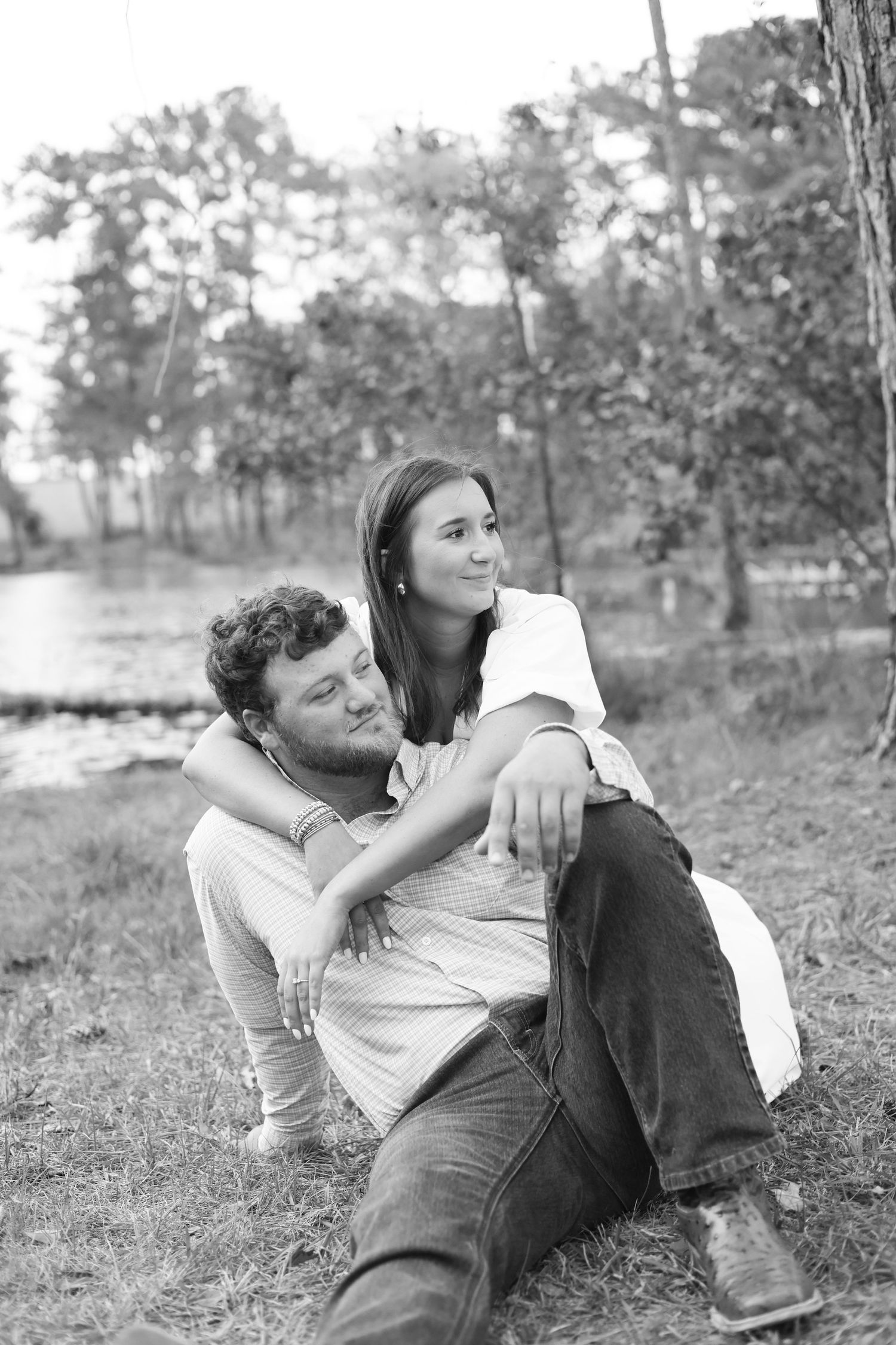 A relaxed black and white portrait of a couple sitting together by a lake.