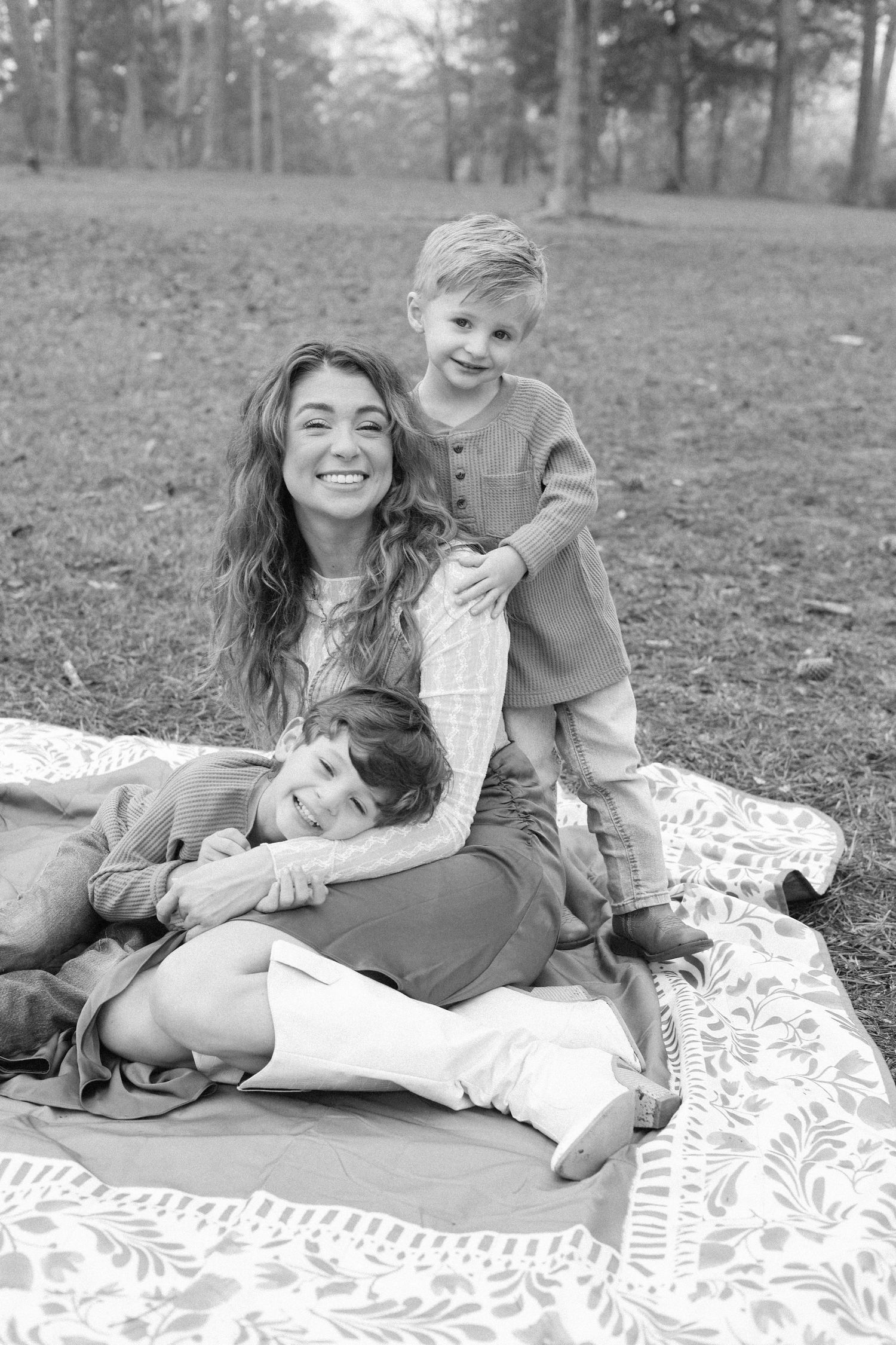 A couple relaxes on a patterned blanket in a grassy outdoor setting, sharing playful and candid moments.
