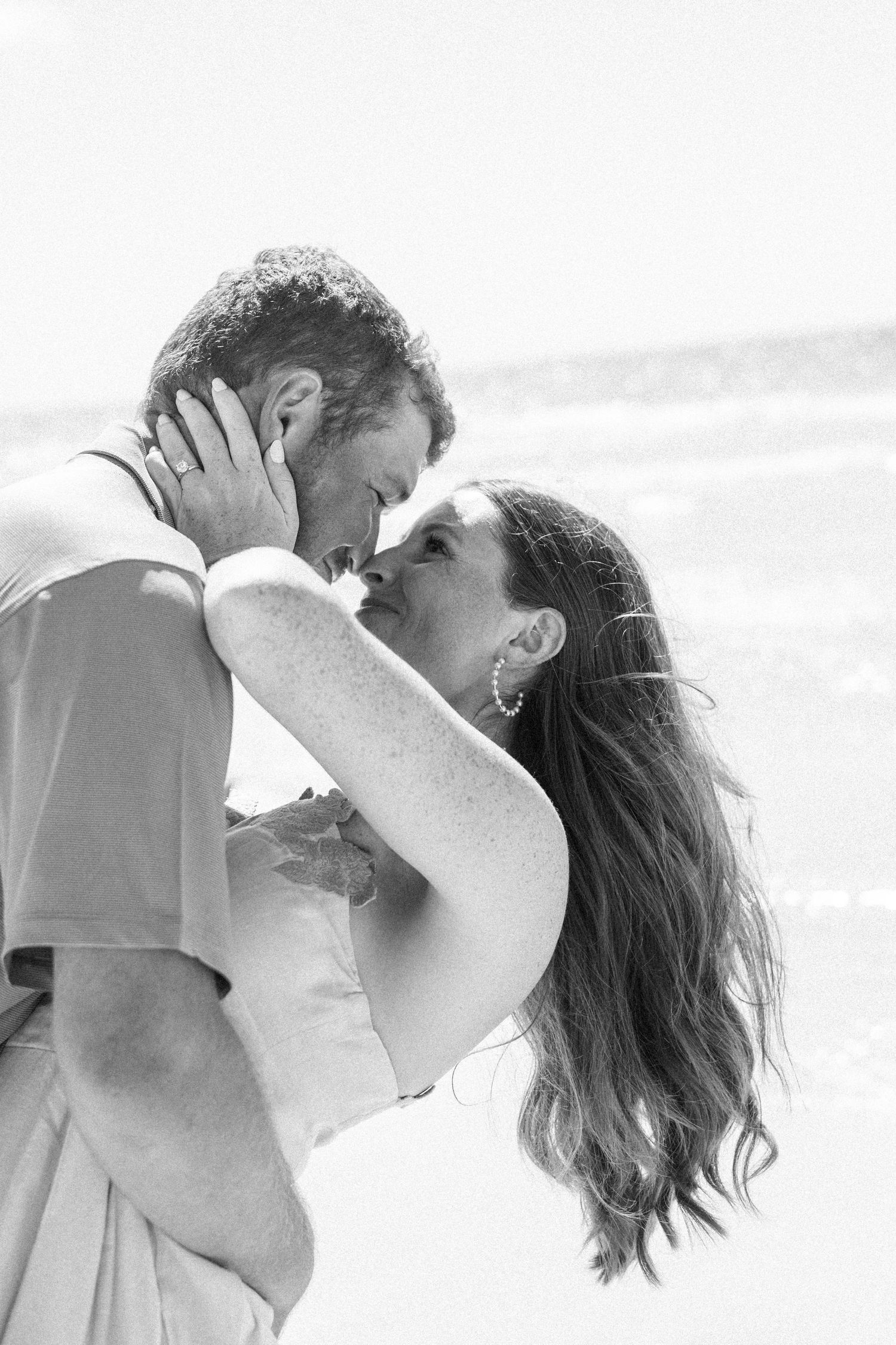 Black and white photo of a bride and groom sharing a romantic kiss on a beach.