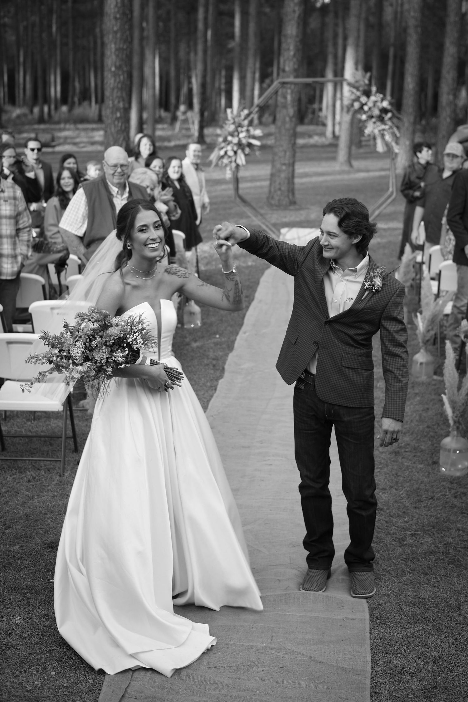 Wedding celebration with joyful dancing on an outdoor pathway among pine trees.