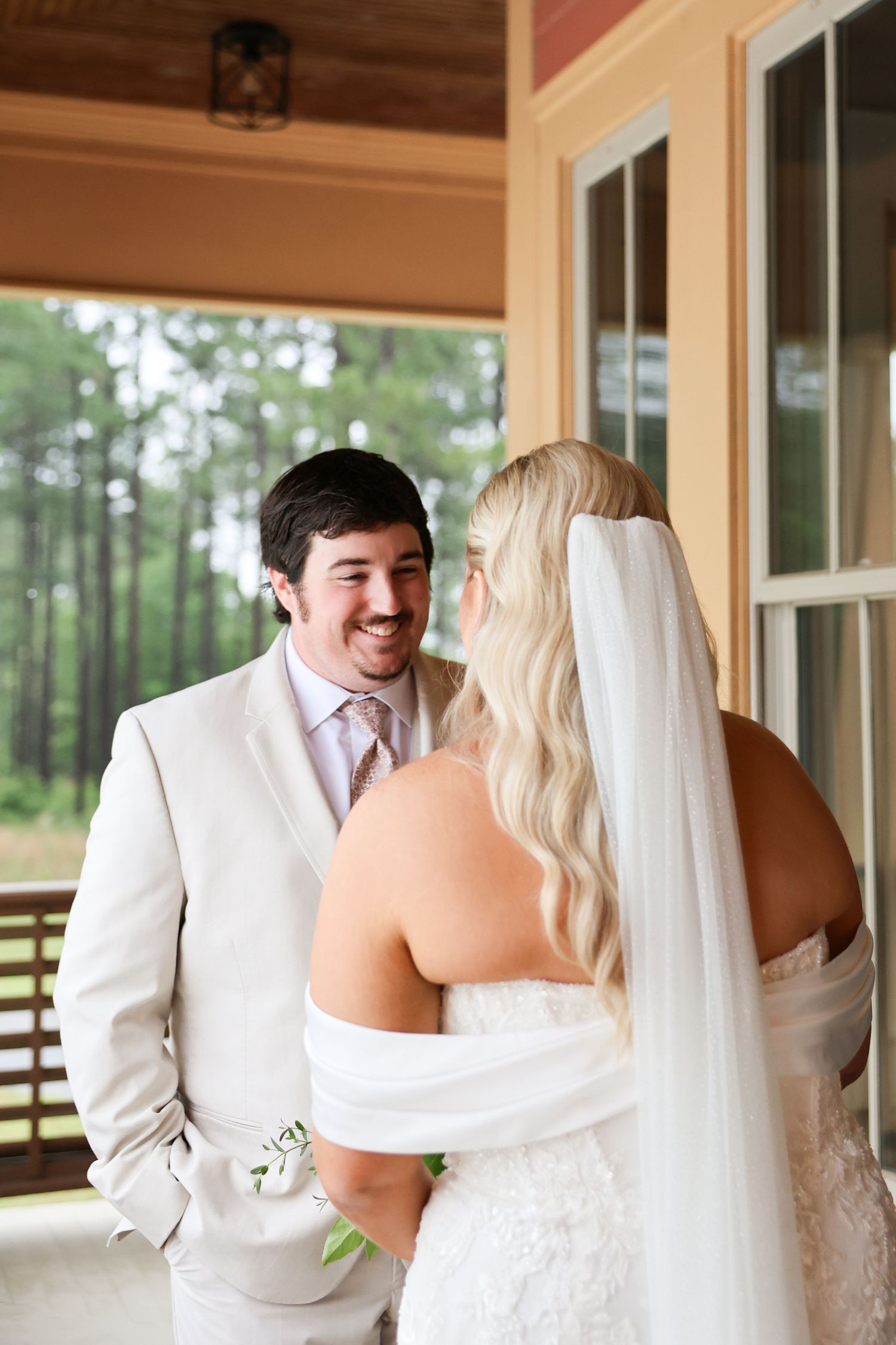 Smiling groom in tan suit sharing first look moment with blonde bride in white wedding dress.