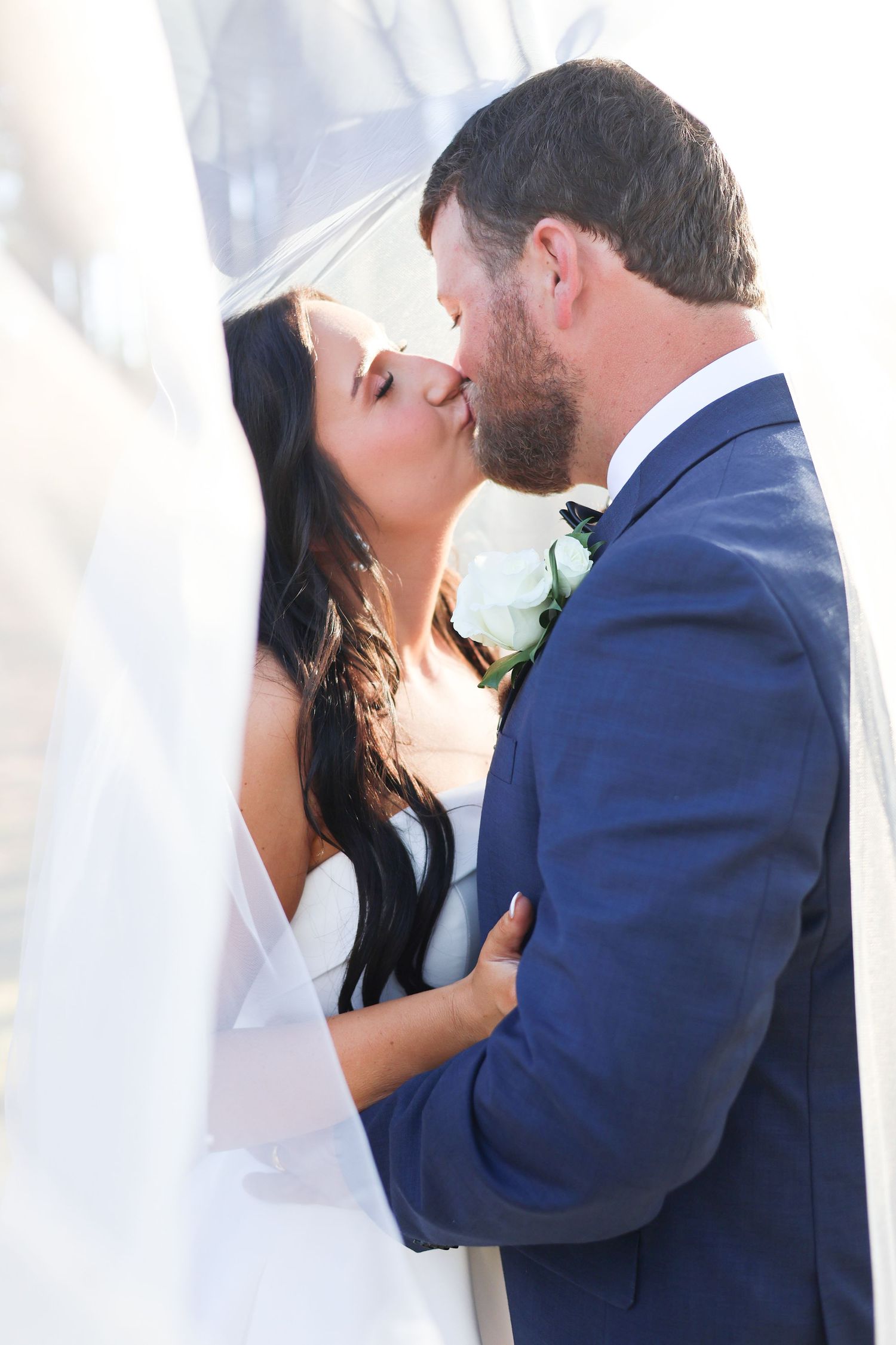 Romantic wedding couple sharing an intimate kiss against a white backdrop.