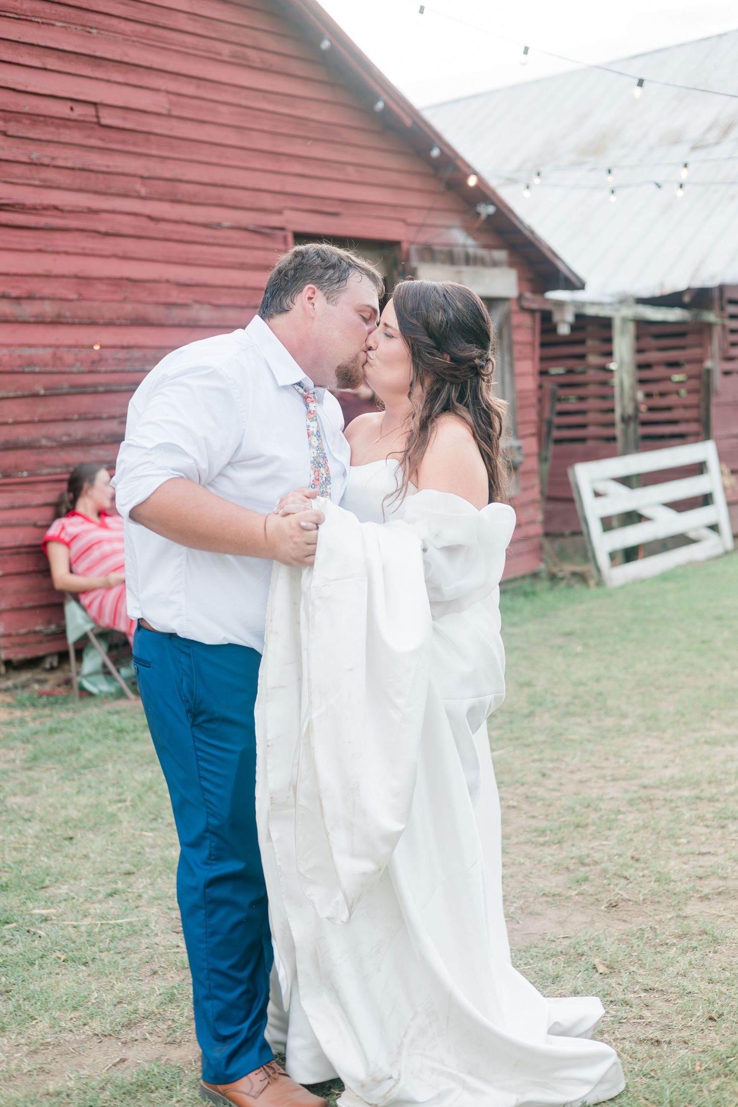 Bride and groom share a romantic kiss outside a rustic red barn at their countryside wedding.