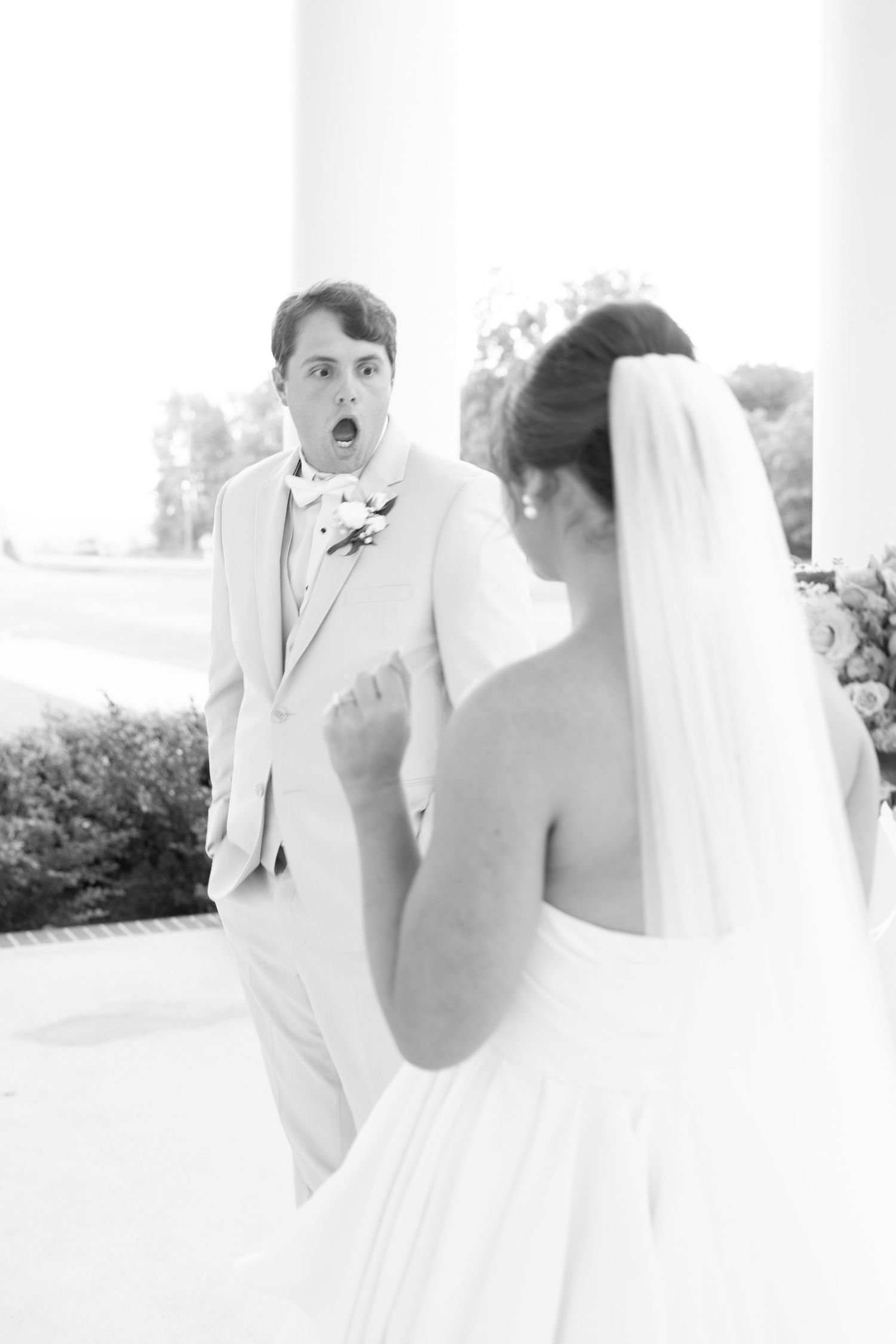 Groom in a tan suit reacts with shock and awe seeing his bride in a white wedding dress for the first time.