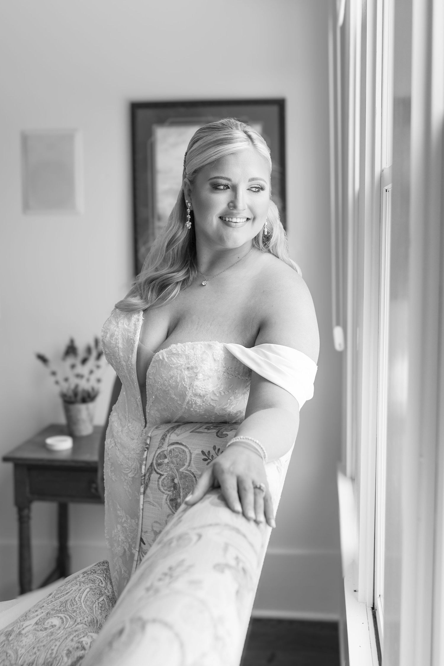 Smiling bride in strapless lace wedding gown leans against staircase railing in elegant black and white portrait.