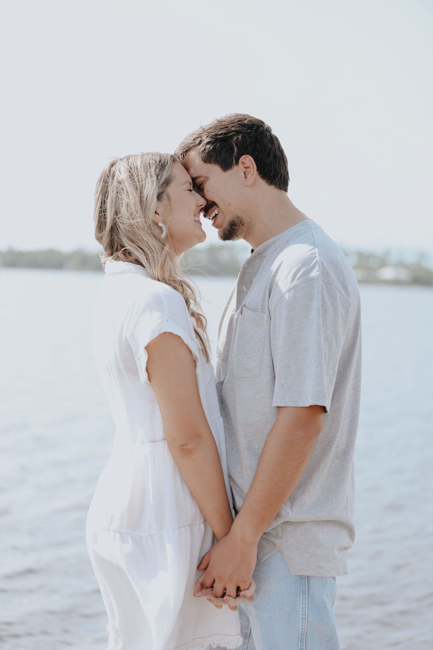 A tender moment between a couple in casual attire against a waterfront backdrop.
