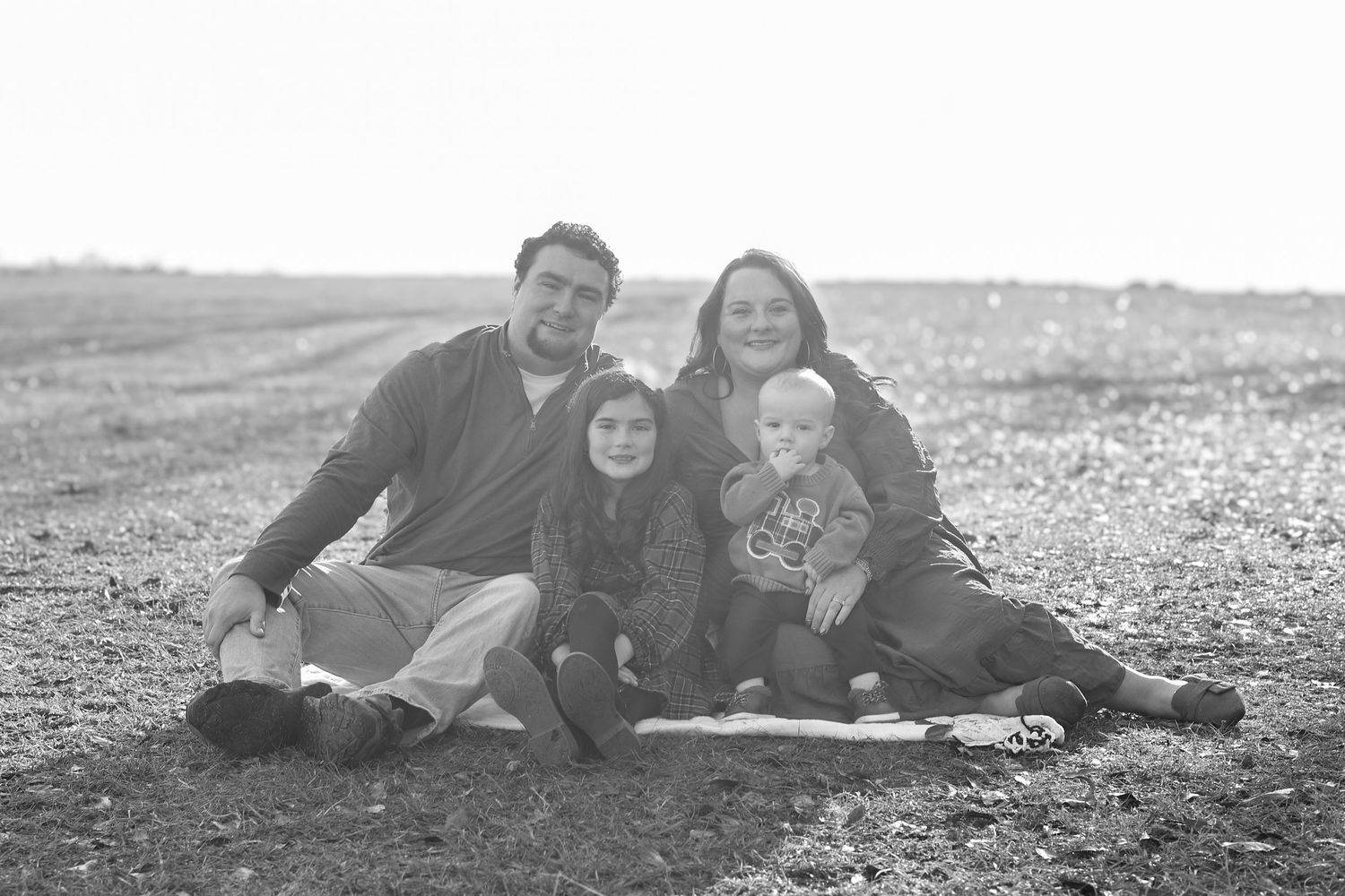 Black and white family portrait of parents with two young children sitting outdoors on rocky ground.